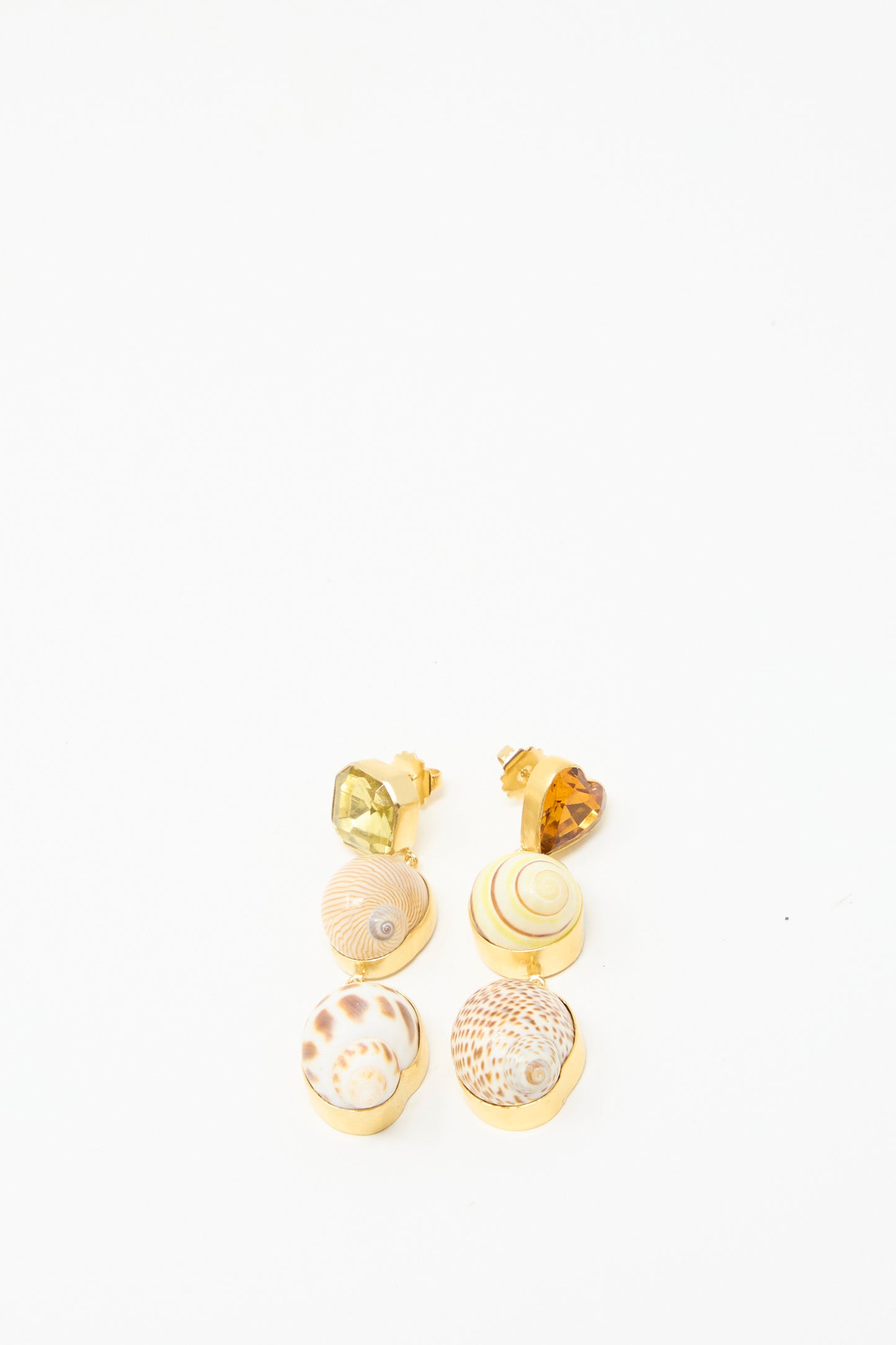 The Shell Charm Drop Earrings by Grainne Morton feature four exquisite mismatched charm drops, made from 18k gold-plated silver. Arranged in a row on a pristine white background, they highlight their ethically sourced allure.