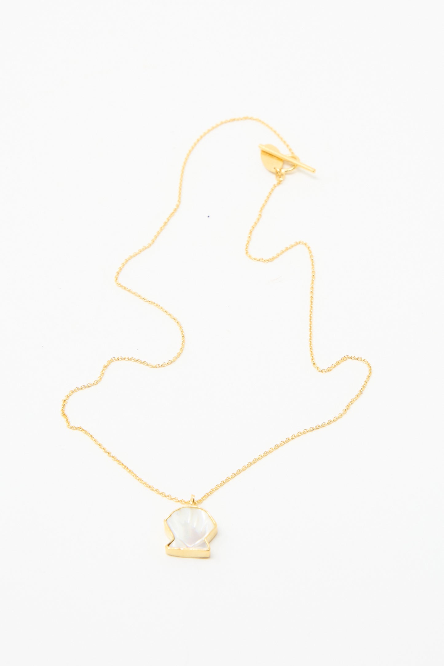 Grainne Morton's Shell Charm Necklace: a gold-plated silver chain with a shell shaped pendant, featuring a white gemstone and displayed on a white background.