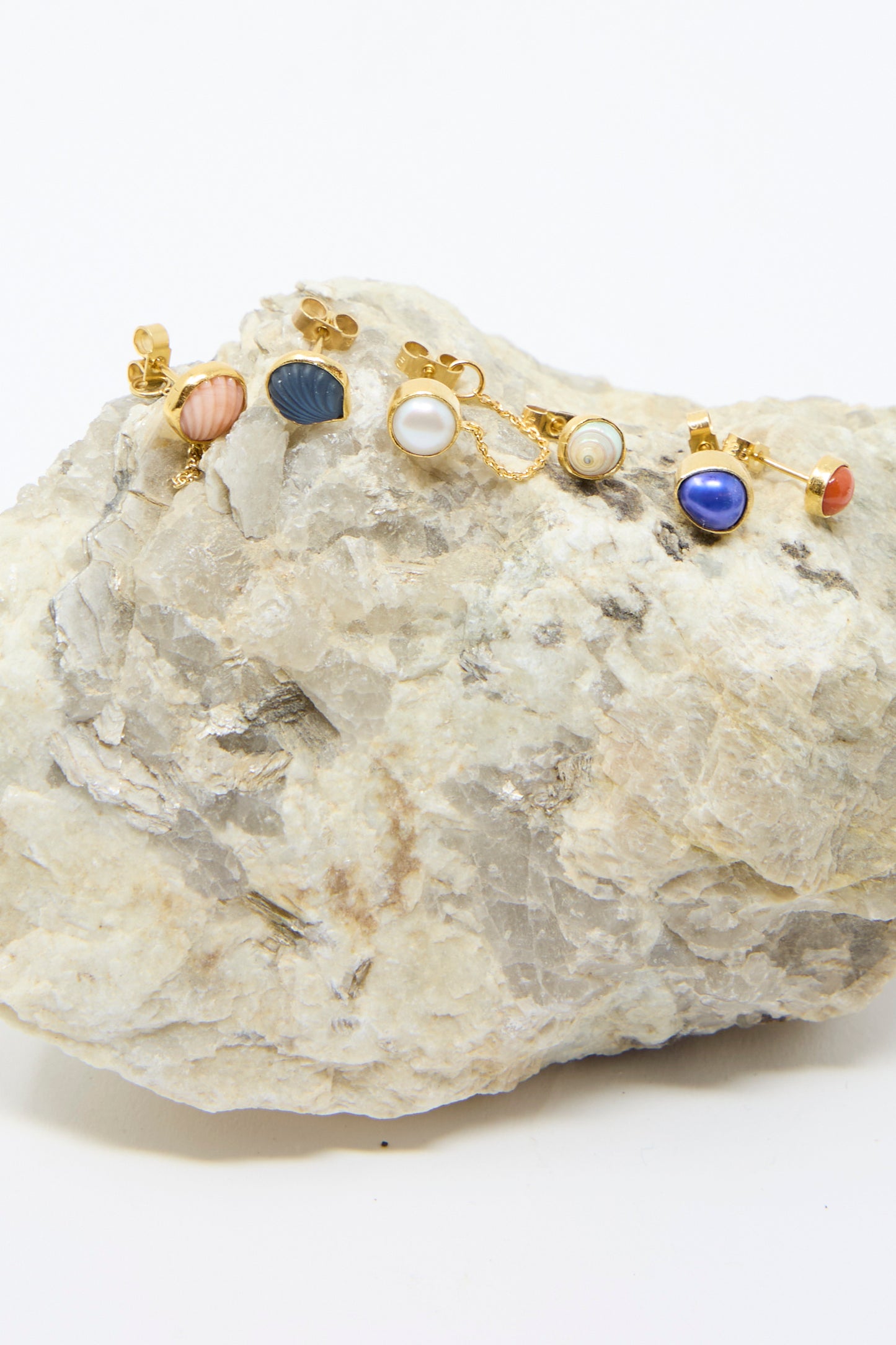 The Stud Earring in Blue Shell by Grainne Morton features ethically sourced stones and 18k gold-plated silver accents, displayed on a textured rock background.