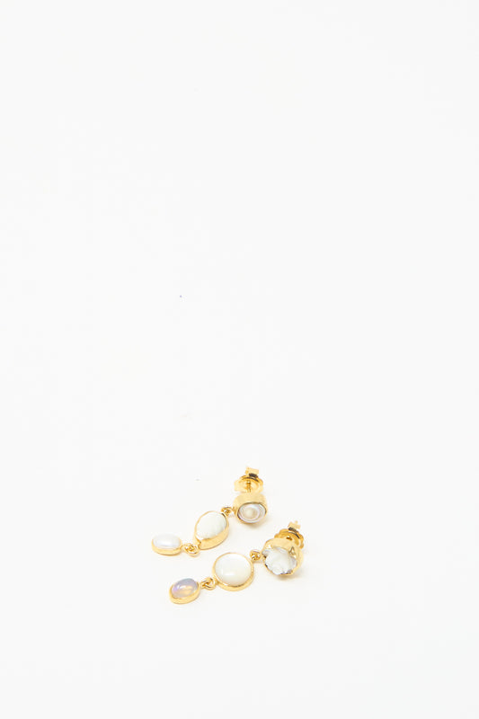 Grainne Morton's Three Charm Moving Drop Earrings are 18k gold-plated and feature iridescent charms with multiple white and lavender stones on a plain white background.