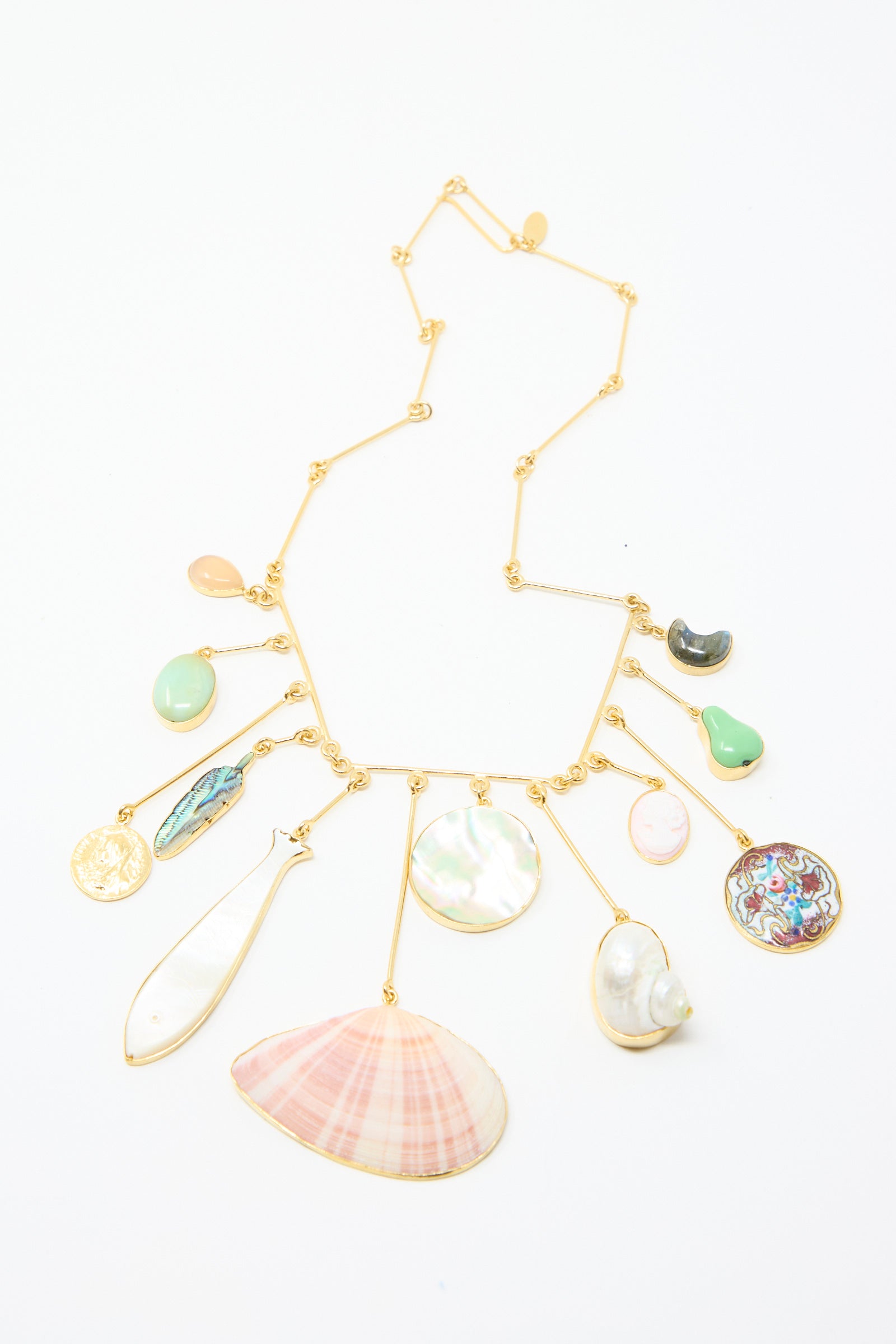 The Wire Charm Drop Necklace by Grainne Morton features an 18k gold-plated silver chain adorned with seashell, semi-precious stone, and coin pendants, all set against a white background.