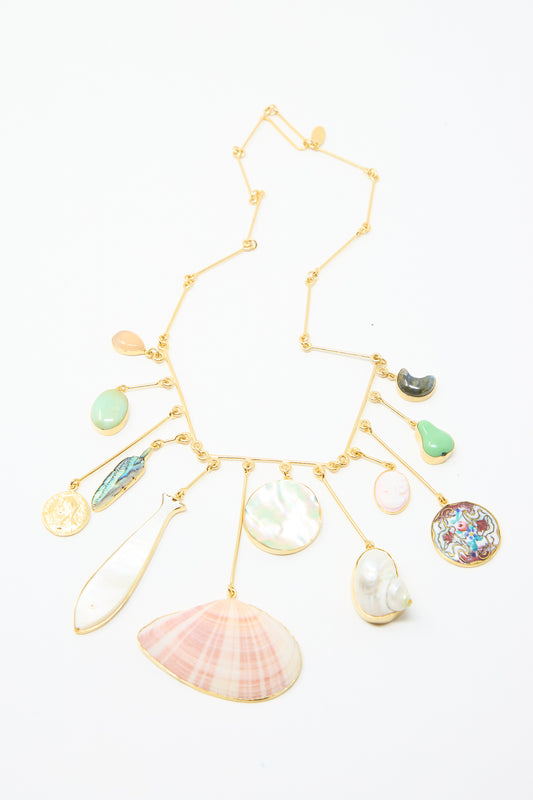 The Wire Charm Drop Necklace by Grainne Morton features an 18k gold-plated silver chain adorned with seashell, semi-precious stone, and coin pendants, all set against a white background.