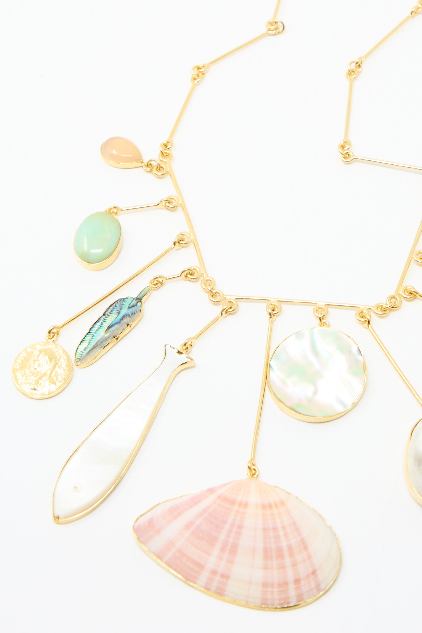 The Wire Charm Drop Necklace by Grainne Morton features a gold-plated silver chain adorned with pendants, including a shell, fish, and semi-precious stones, against a white backdrop. 