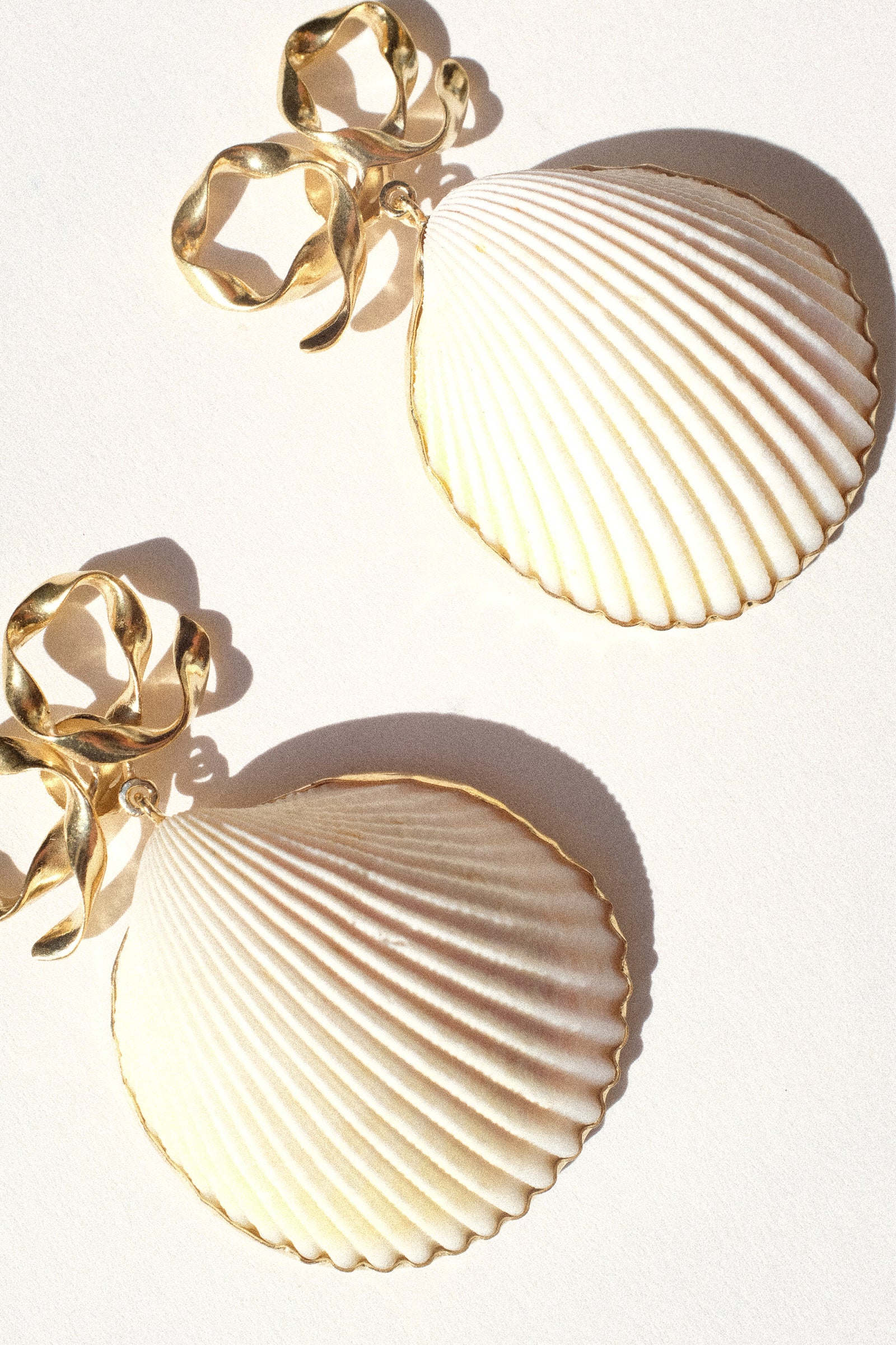 Gold bow and shell earrings by Grainne Morton, on a white background