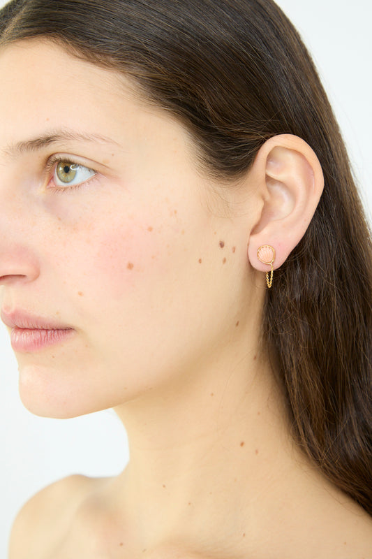 A woman with long brown hair displays Grainne Morton's Chain Stud Earring in Pink Shell, resembling a vintage coral rope design, on her left ear against a plain white background.