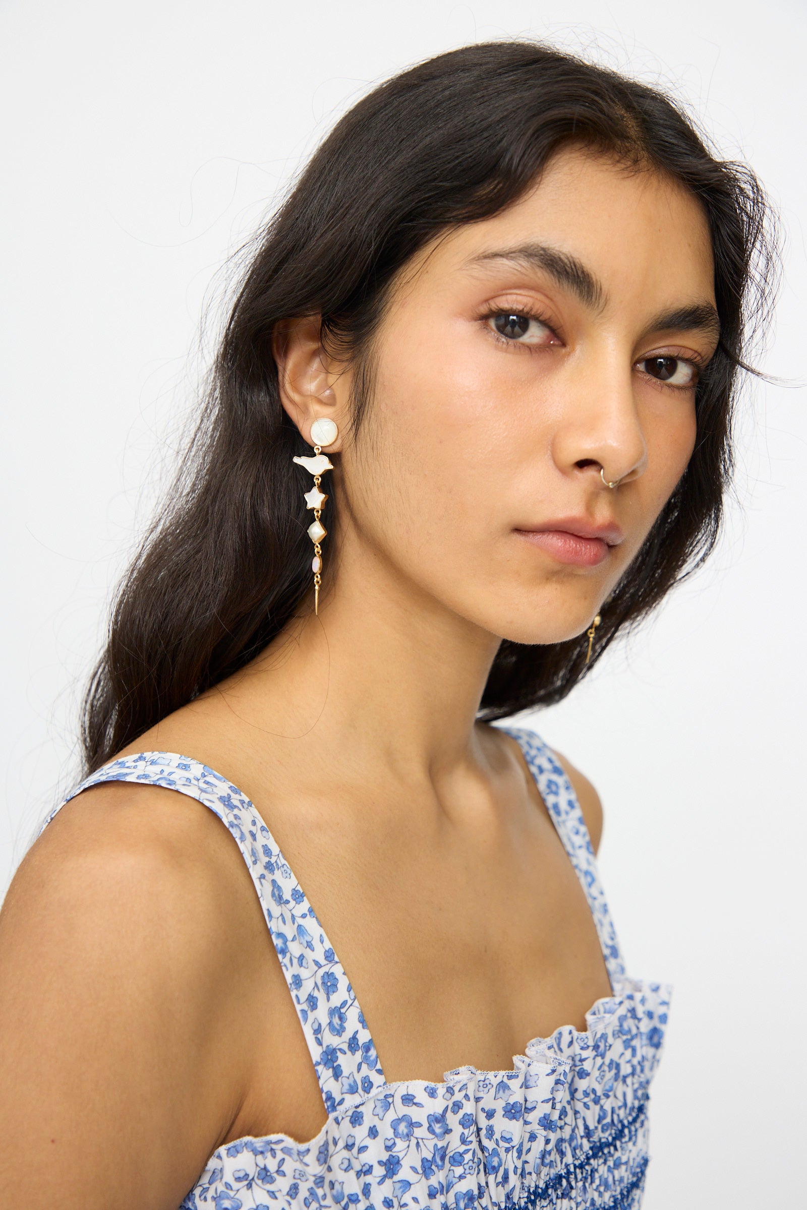 Woman with long dark hair wears Grainne Morton's Five Charm with Victorian Drop Earrings and a blue floral sleeveless top, looking at the camera against a plain background.