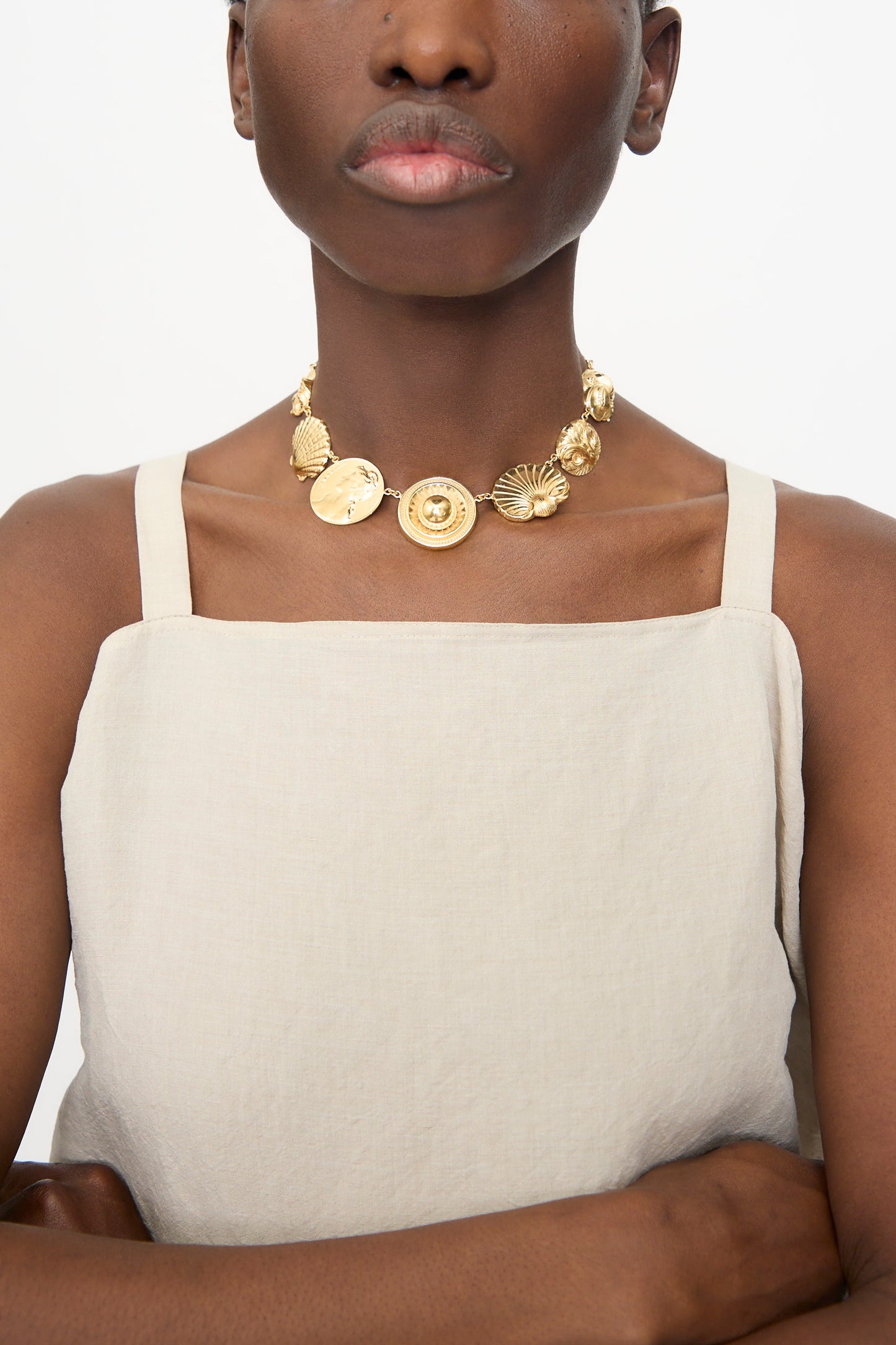 A person wearing a beige square-neck top and the Grainne Morton Gold Button Necklace, photographed from the shoulders up against a plain background.