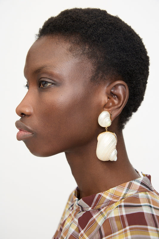 A person with short curly hair wears Grainne Morton Moon and Star Shell Drop Earrings and a plaid shirt, shown in profile against a plain background.