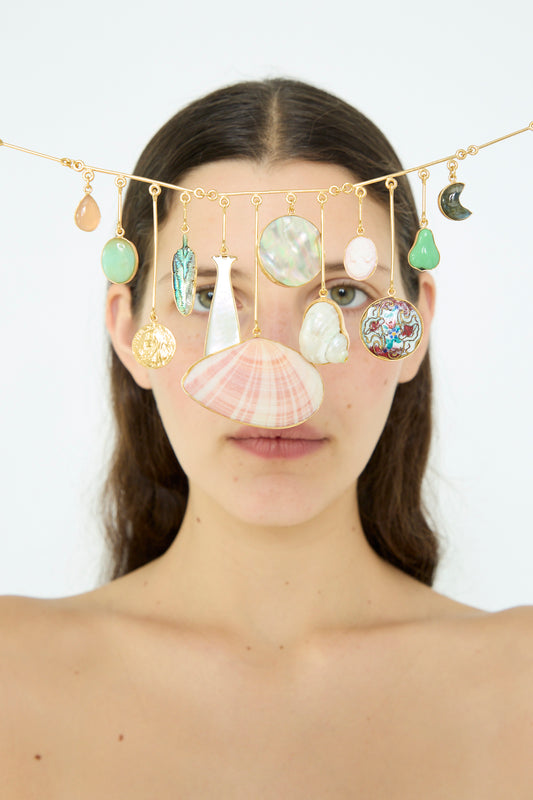 A woman stands behind an array of Wire Charm Drop Necklaces by Grainne Morton, featuring seashell and semi-precious stone pendants, against a plain background.