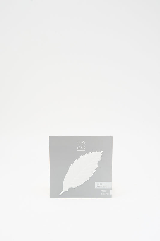 A square package of Paper Leaf Winter Incense in Cedar, featuring a white leaf-shaped Japanese incense labeled “No. 03 Cedar.”