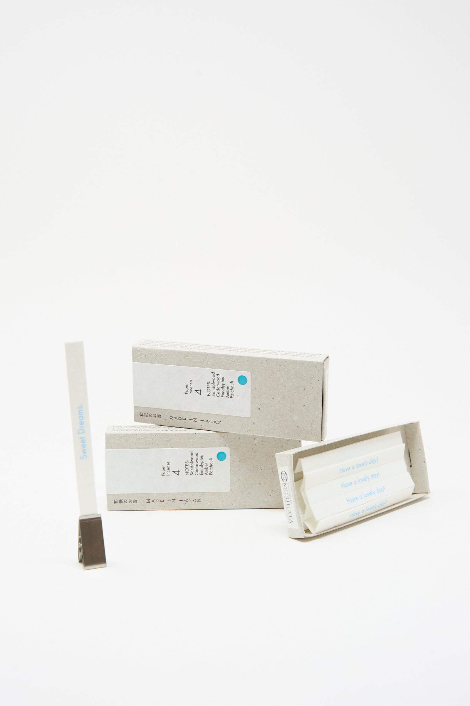 Three rectangular boxes and a holder display Morihata’s Washi Paper Incense Strips in Mellow Grove—one open box reveals strips labeled "Have a lovely day." Made in Japan, these infuse your space with natural aromas. Arranged on a white background.