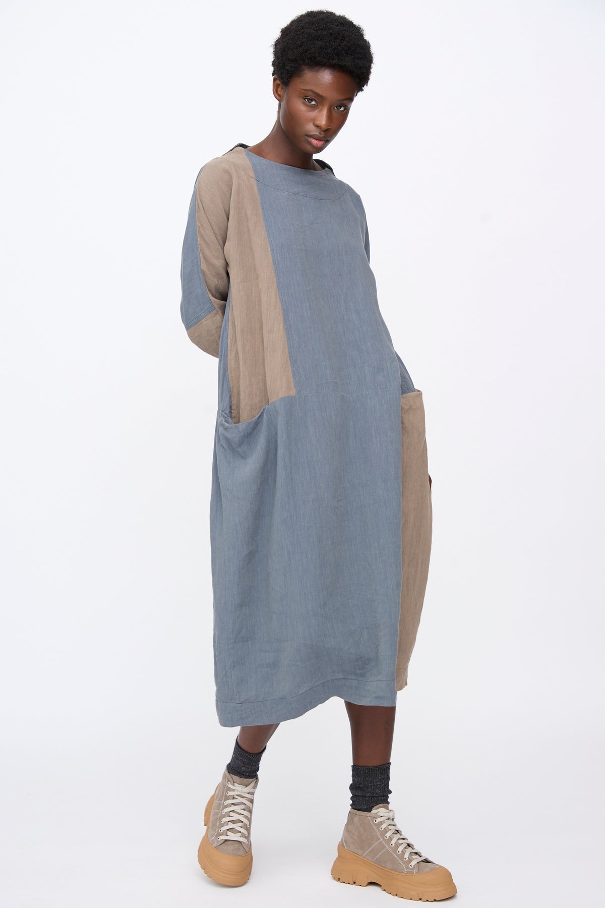 A person wearing the Hallelujah Berger des Montagne de la Castille Dress in Blue Mix, a color-blocked linen blend robe styled with grey socks and tan platform sneakers.