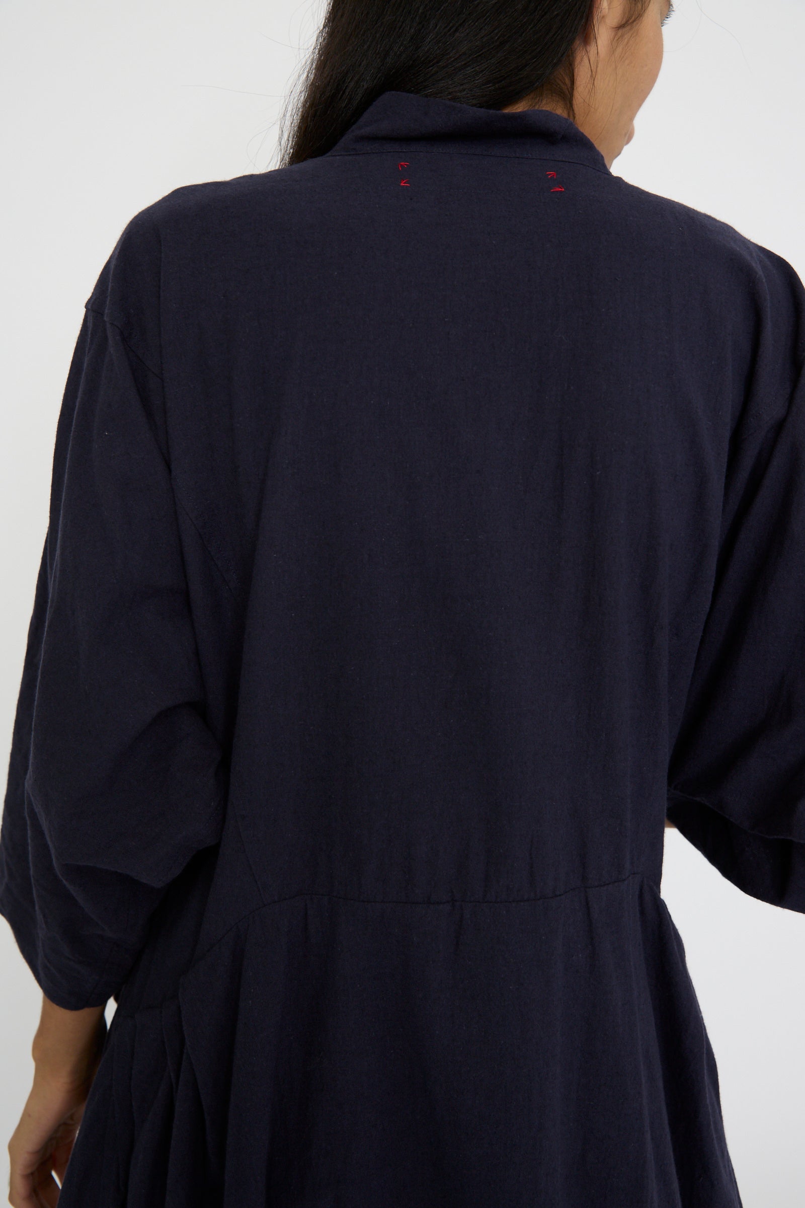 A person wearing the Canvas Acolyte Robe in Navy by Hallelujah, a dark blue garment featuring a relaxed fit with bell sleeves is seen from the back.