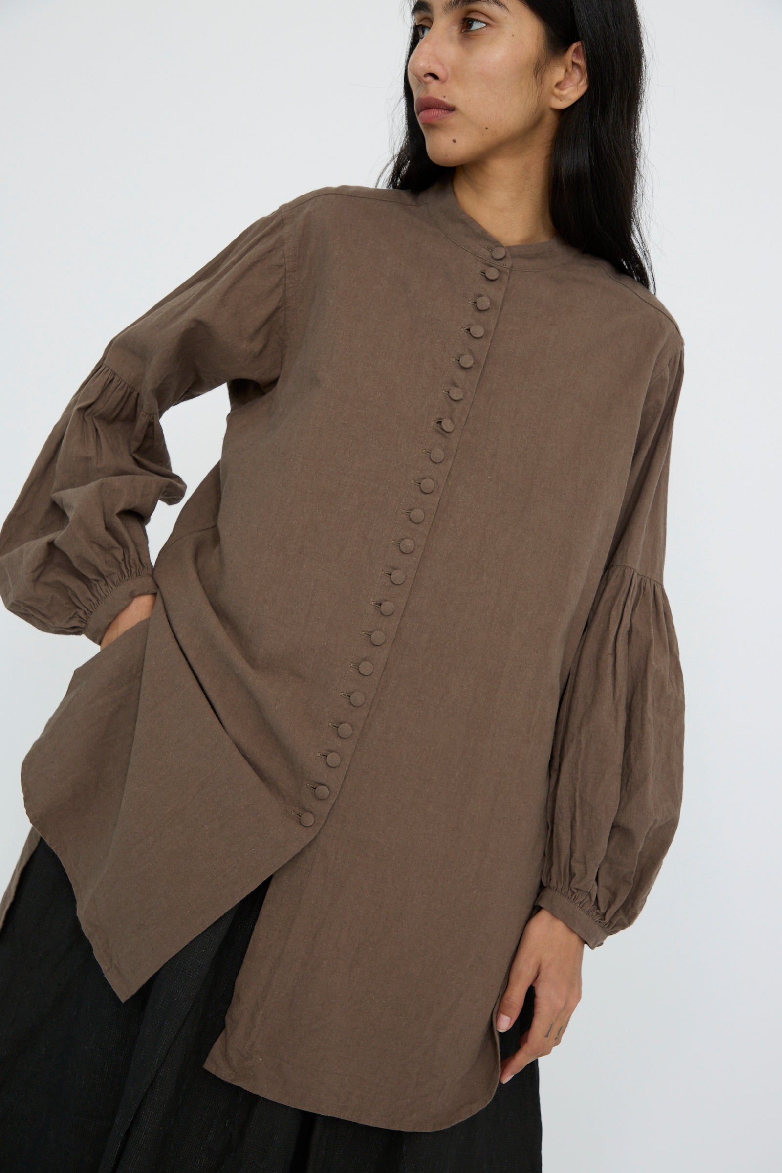 A person wearing the Canvas Chemise Religieuse in Chocolate by Hallelujah features button details, an asymmetrical design, and a sophisticated band collar.