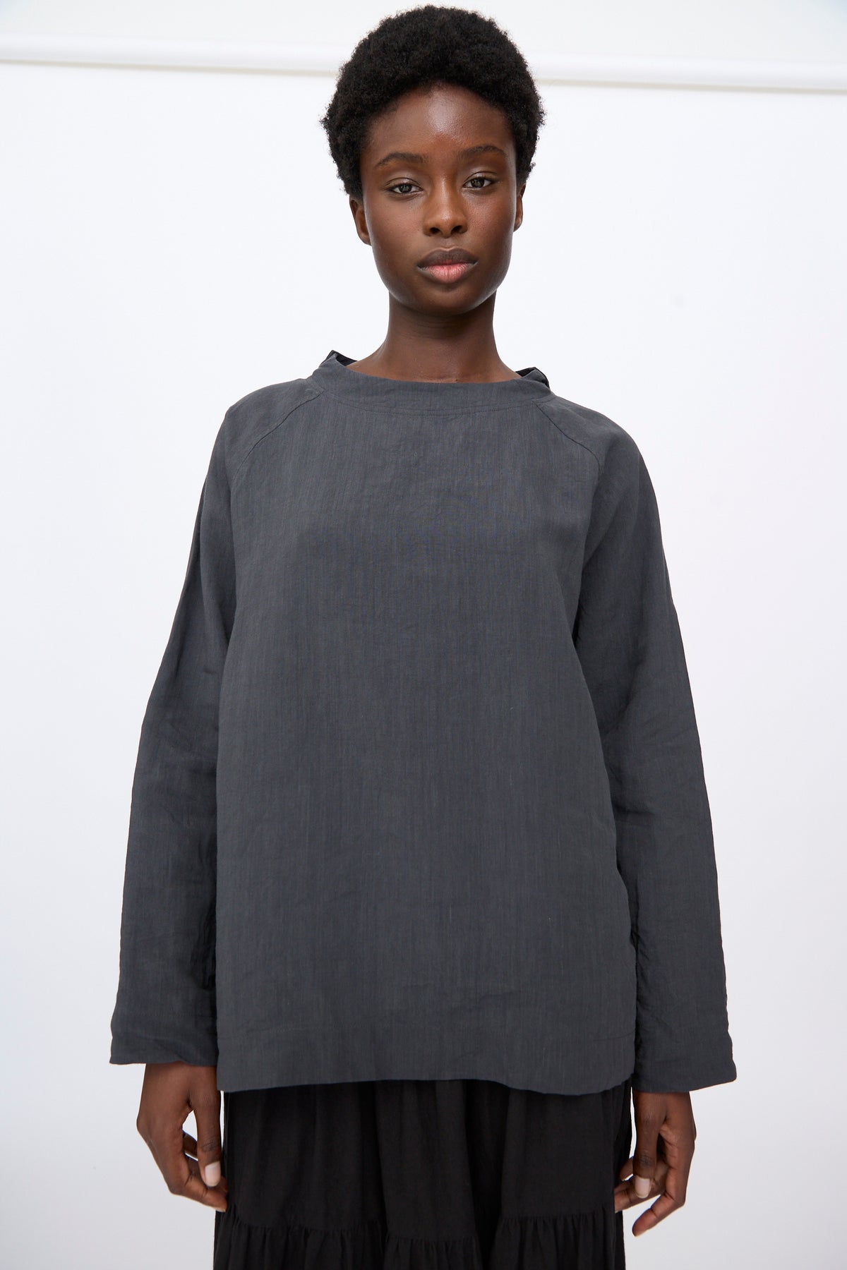 A person wears a gray, long-sleeved, linen blend Chemise de Berger tunic over a black skirt.
