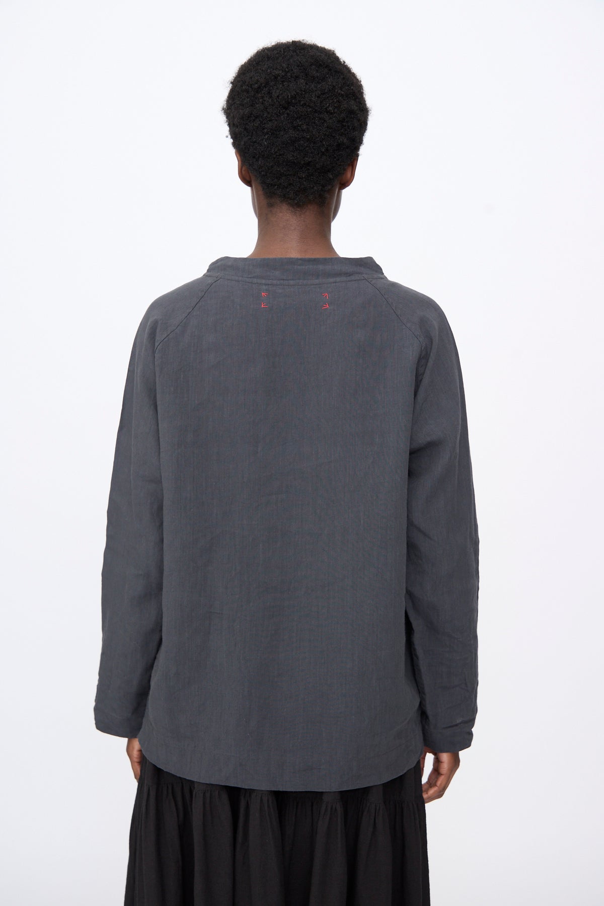 Back view of a person wearing a charcoal gray, linen blend Hallelujah Chemise de Berger in Gray long-sleeve shirt with small red stitch details at the neckline.