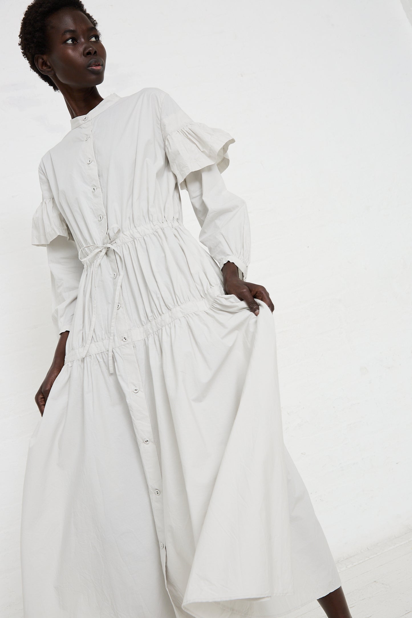 A person wearing a long, white Cotton Chemise à la Reine in Turnip with ruffled sleeves by Hallelujah, handmade in Kyoto using vegetable dyes, poses against a plain white background.