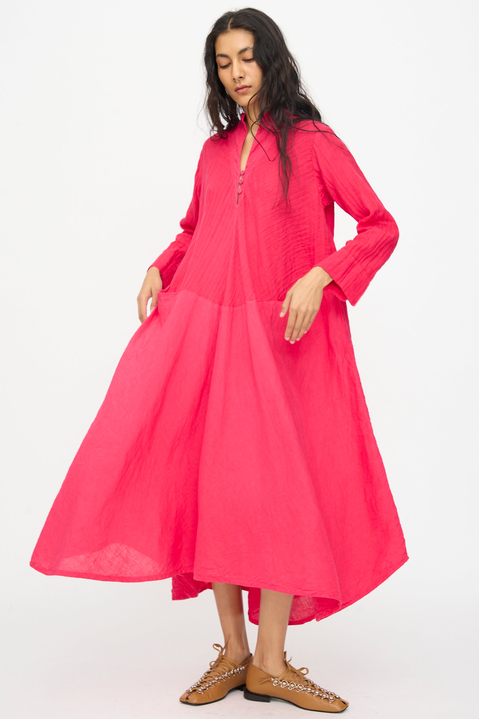 A woman wears the Hallelujah Cotton Linen Robe de Femme de Chambre in Cherry Red, a loose-fitting, long-sleeve maxi dress with a collar and front zipper, paired with brown flats, standing against a white background.