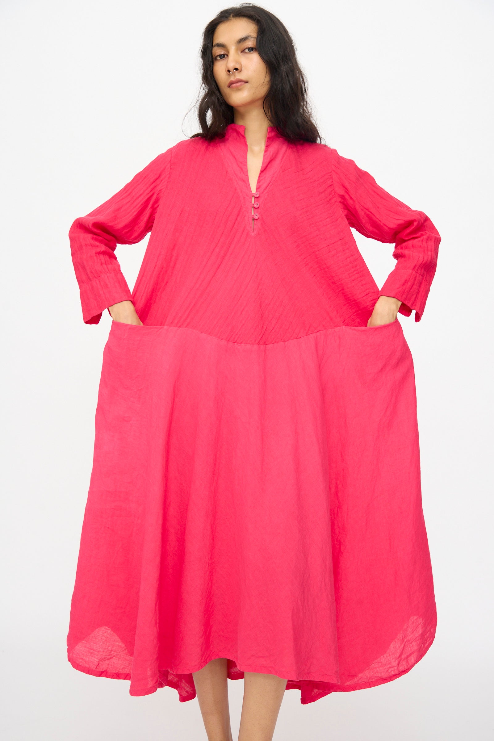 A person stands against a white background wearing the Hallelujah Cotton Linen Robe de Femme de Chambre in Cherry Red, featuring long sleeves, a high collar, front buttons, and side pockets.