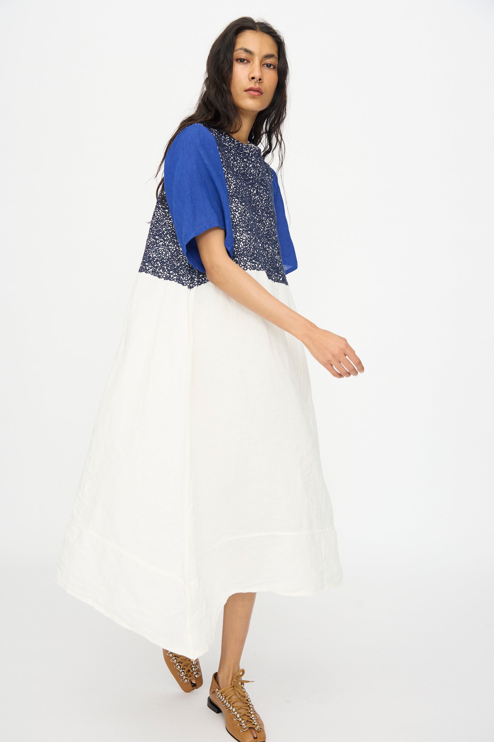 A woman in the Hallelujah French Linen La Pucelle Dress in Off White Navy Stitch, paired with brown sandals, stands against a plain white background.