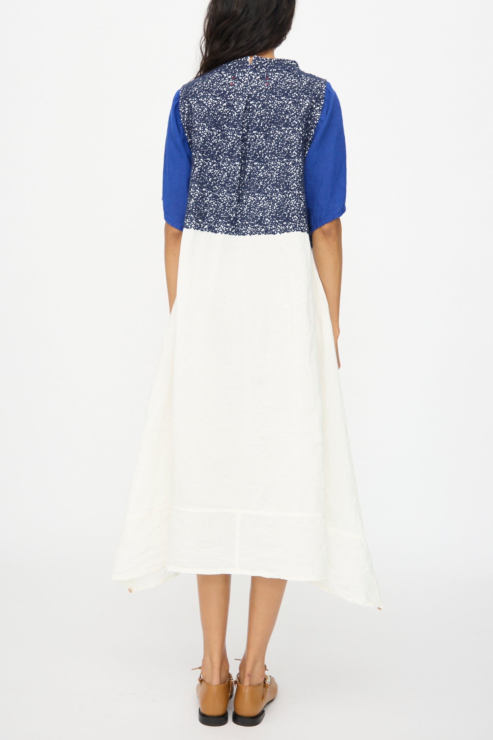 A woman, seen from behind, wears the Hallelujah French Linen La Pucelle Dress in Off White Navy Stitch—made in Japan—with a blue patterned top, solid blue sleeves, and a white skirt. She pairs it with sandals.