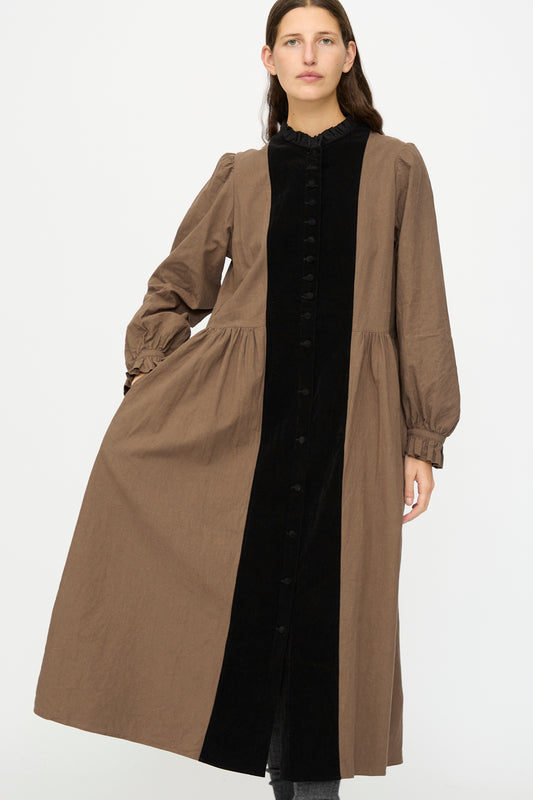A person models the Hallelujah Jeune Paysanne in Chocolate and Black, a long velveteen cotton dress with a black buttoned front panel, standing against a plain white background.
