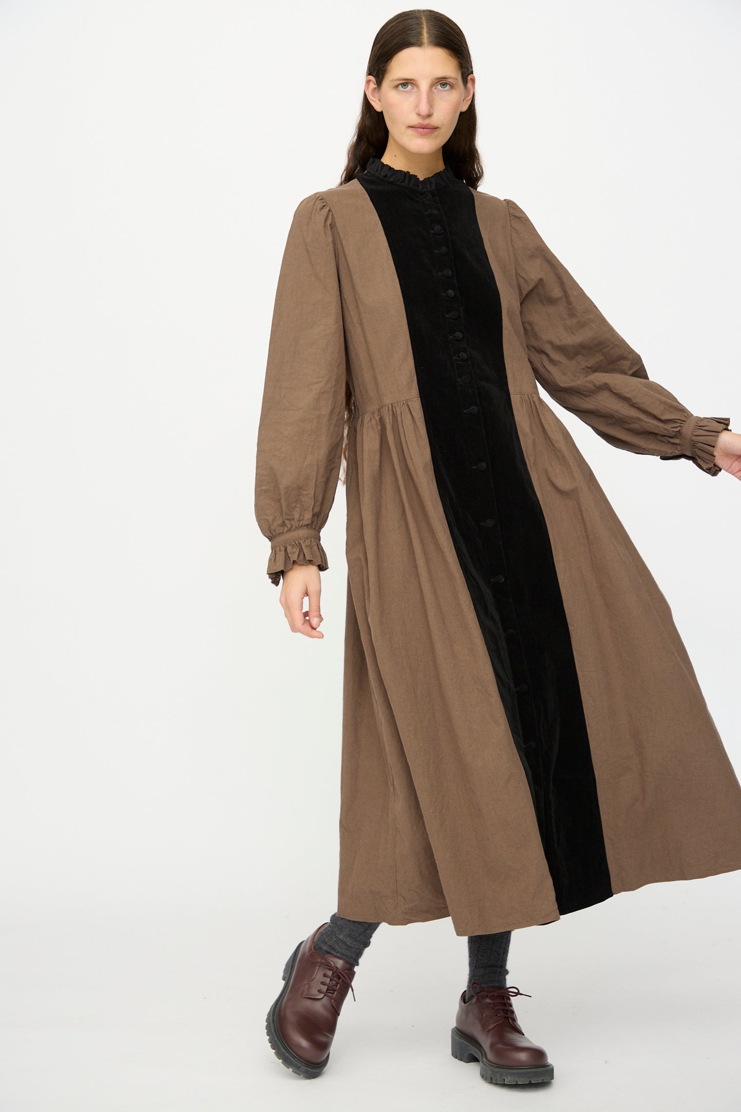 A woman models Hallelujah's "Jeune Paysanne in Chocolate and Black," featuring a long brown velveteen cotton dress with a ruffle collar, black front panel, long sleeves, and dark brown lace-up shoes against a white background.