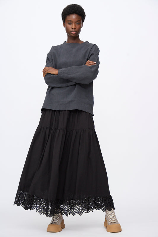 A person wears a long-sleeved dark grey top, a black Linen Cotton Jupe in Black A-line midi skirt with a lace hem, and beige platform sneakers.