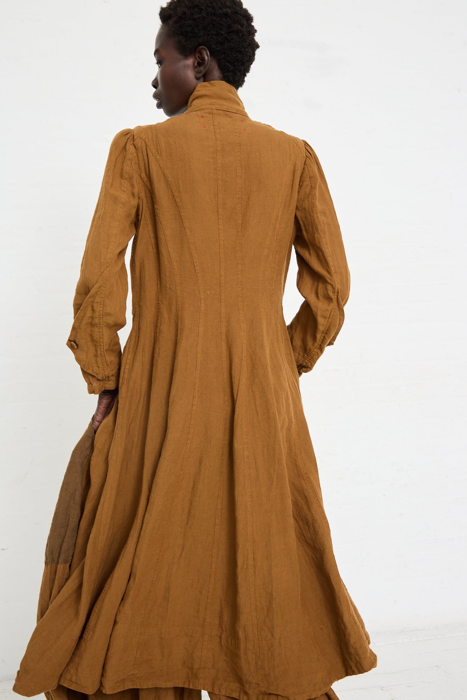 Person wearing a Hallelujah Linen Manteau de Pompier 1800's in Coffee with a high collar, made using a unique dyeing process in Kyoto, seen from the back, standing against a white background.