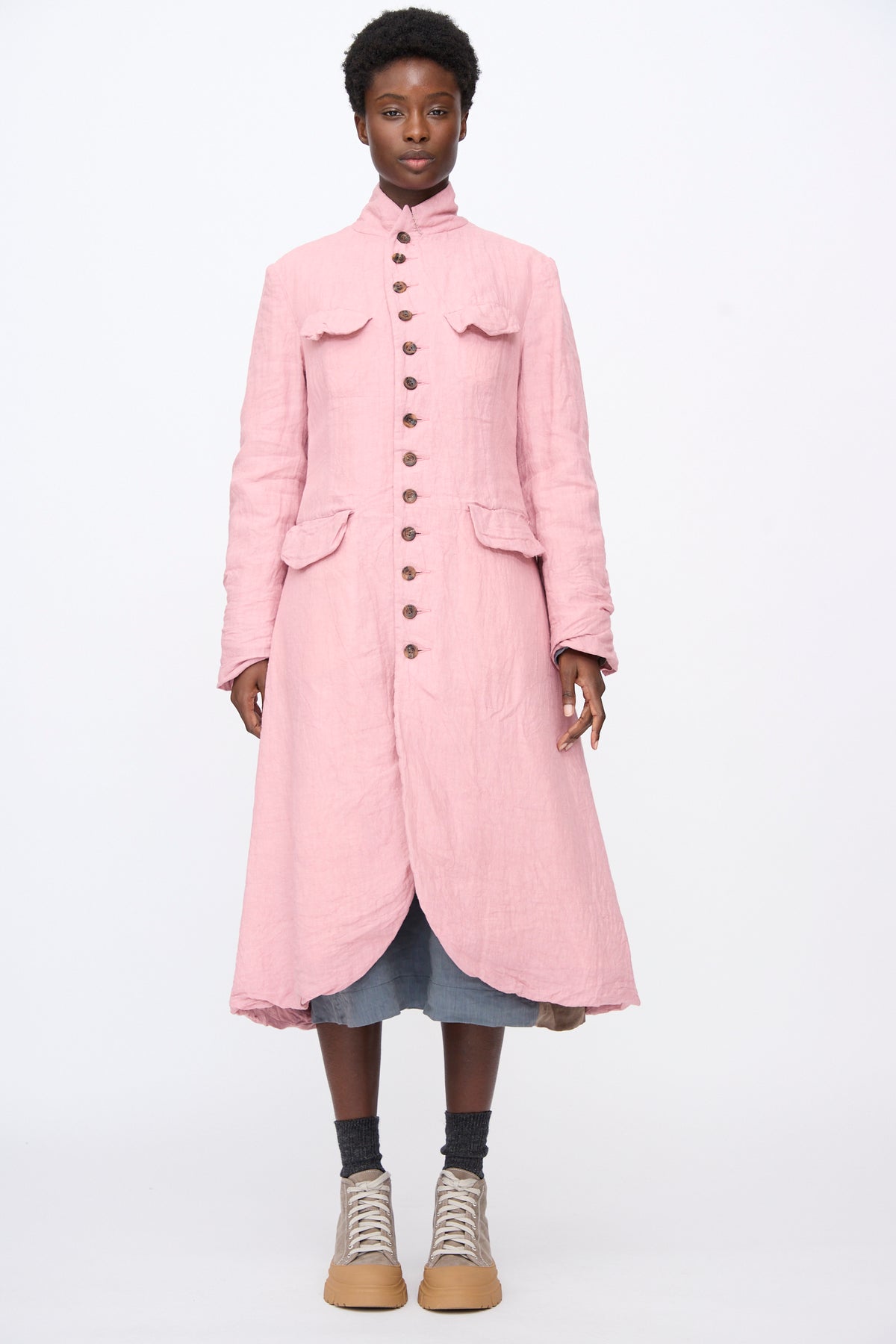 A model wears a Hallelujah Linen Manteaux de Chasse in Pink, a long-sleeved, relaxed fit button-down linen hunting coat with chest and hip pockets.
