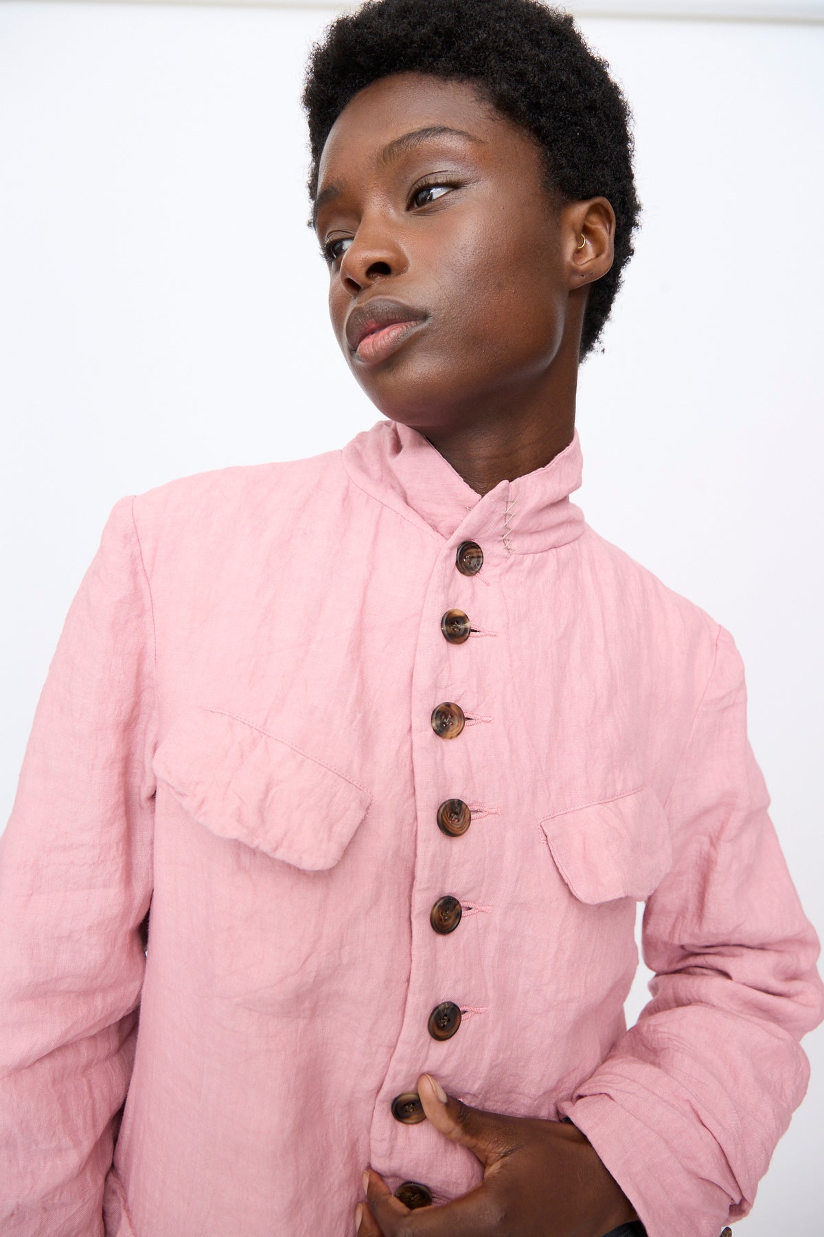A model wearing a Hallelujah Linen Manteaux de Chasse in Pink, a relaxed fit, light pink, button-up jacket with a high collar and two chest pockets.