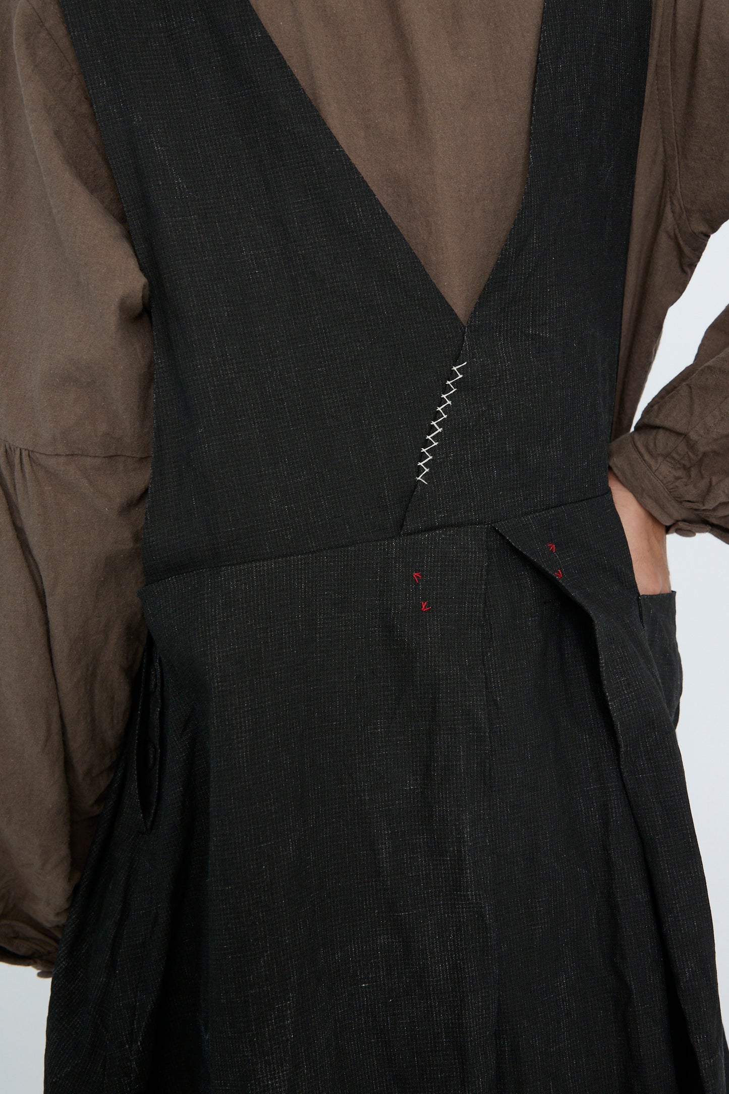 Close-up of a person wearing Hallelujah's Linen Priest's Tablier in charcoal black over a brown shirt, featuring textured linen with red accents and visible stitching on the back.