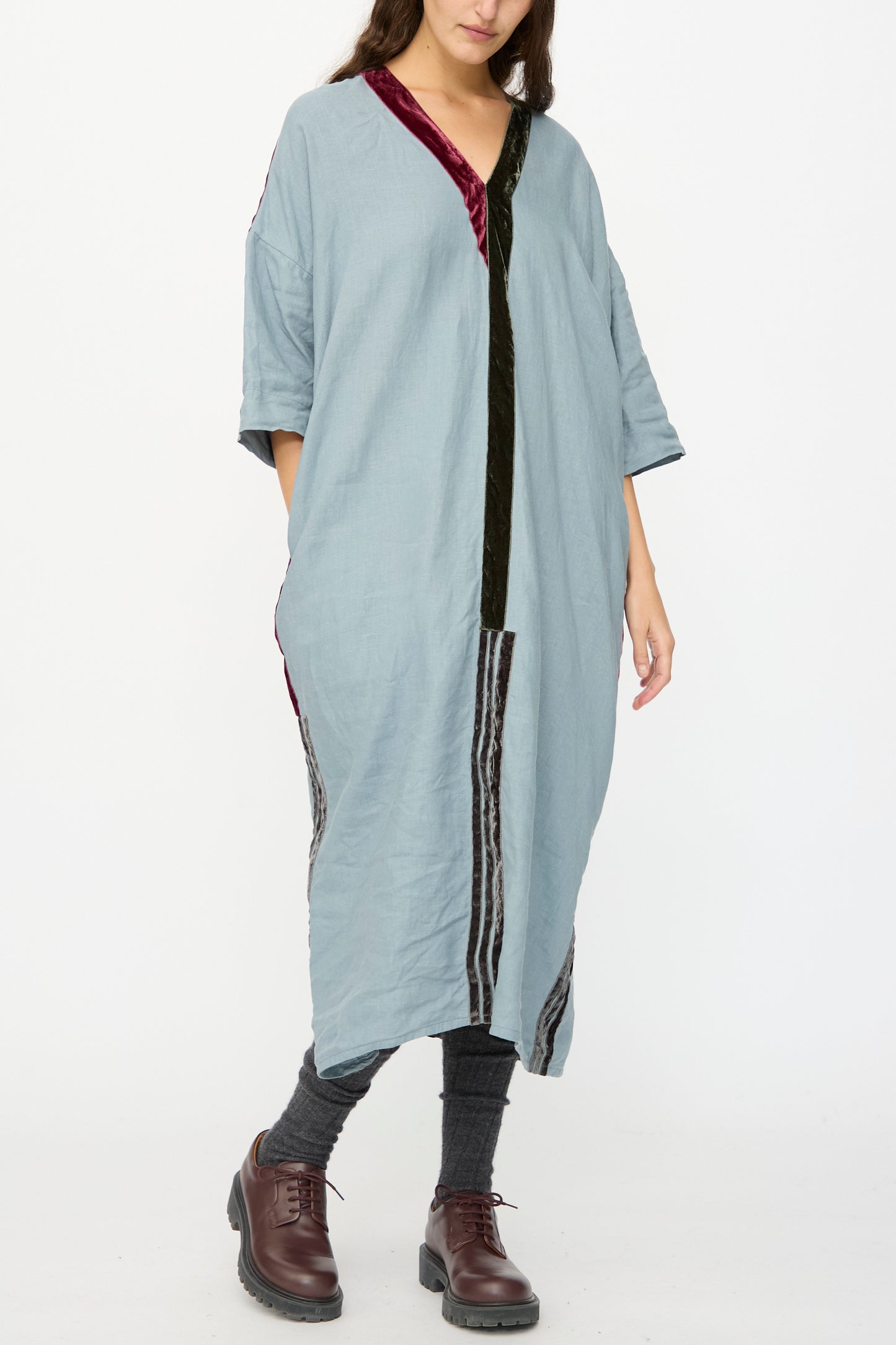 A person wearing the Hallelujah Linen Robes de couture 1930s in Blue, paired with gray leggings and brown lace-up shoes, stands against a plain white background.