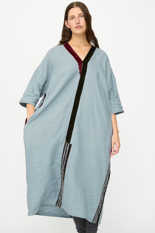 A woman wears the Hallelujah Linen Robes de couture 1930s in Blue, featuring a relaxed fit, black and burgundy velvet trim, and three-quarter sleeves, standing against a plain white background.