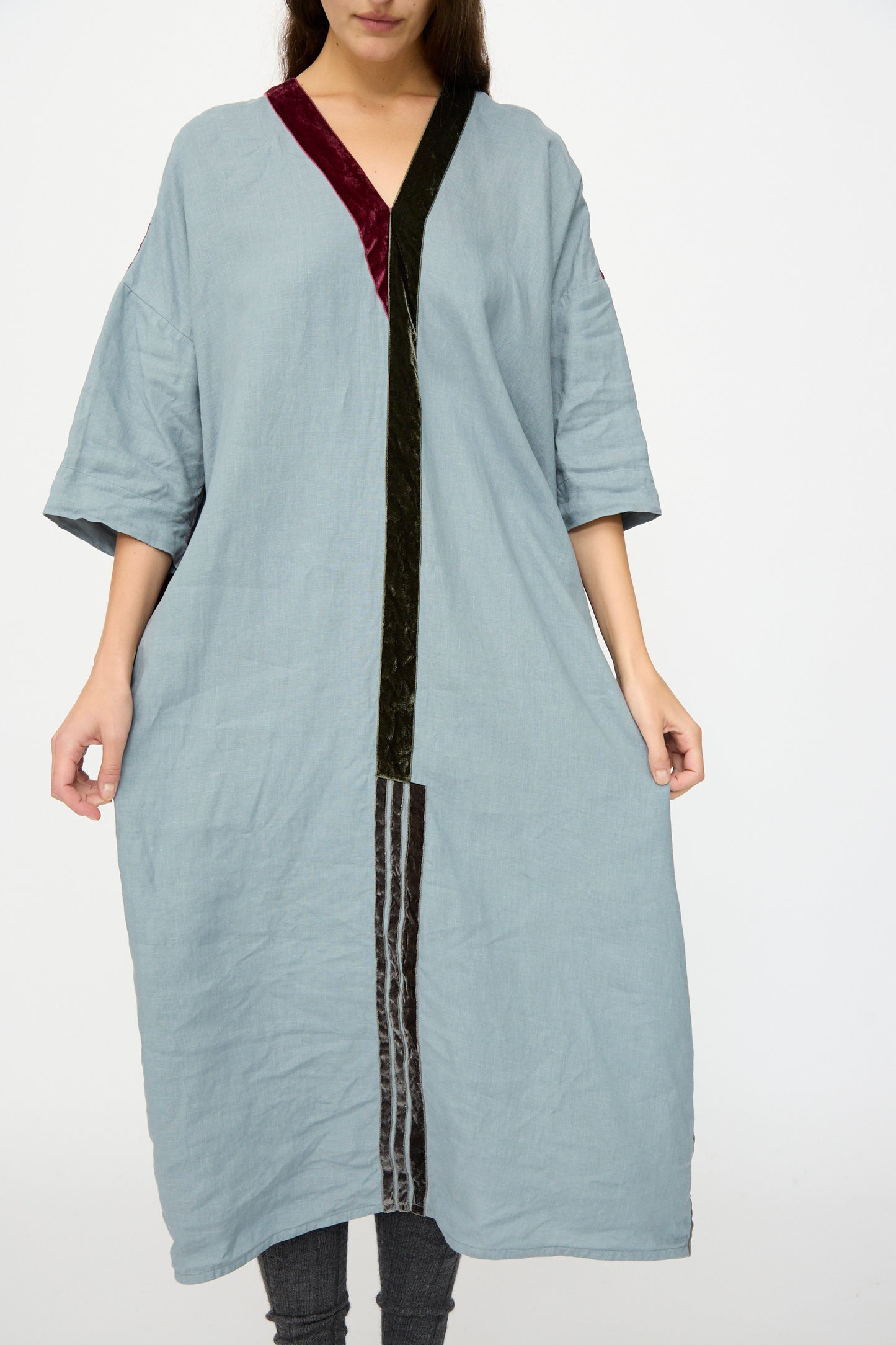 A woman wears the Hallelujah Linen Robes de couture 1930s in Blue—a relaxed fit, light blue linen dress with three-quarter sleeves and burgundy-black velvet trim—standing against a plain white background. Made in Japan.