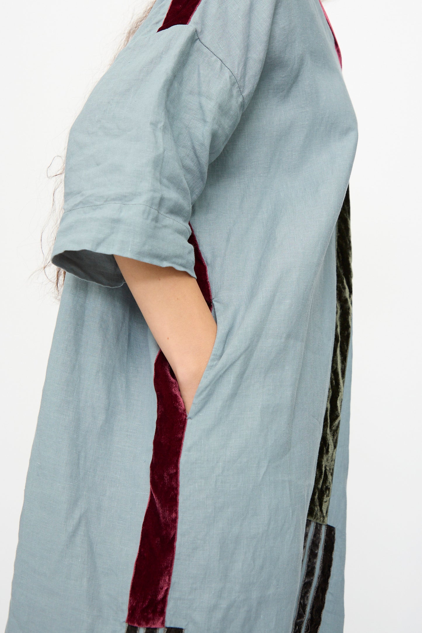 Model wears the Hallelujah Linen Robes de couture 1930s in Blue, a relaxed fit linen dress featuring red and dark green velvet accents, standing with one hand in her pocket.