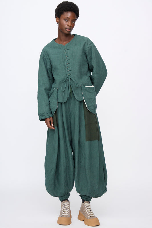 A person wearing a green Linen Veste de Berger with patch pockets and matching loose-fitting, wide-leg trousers, paired with light-colored sneakers.