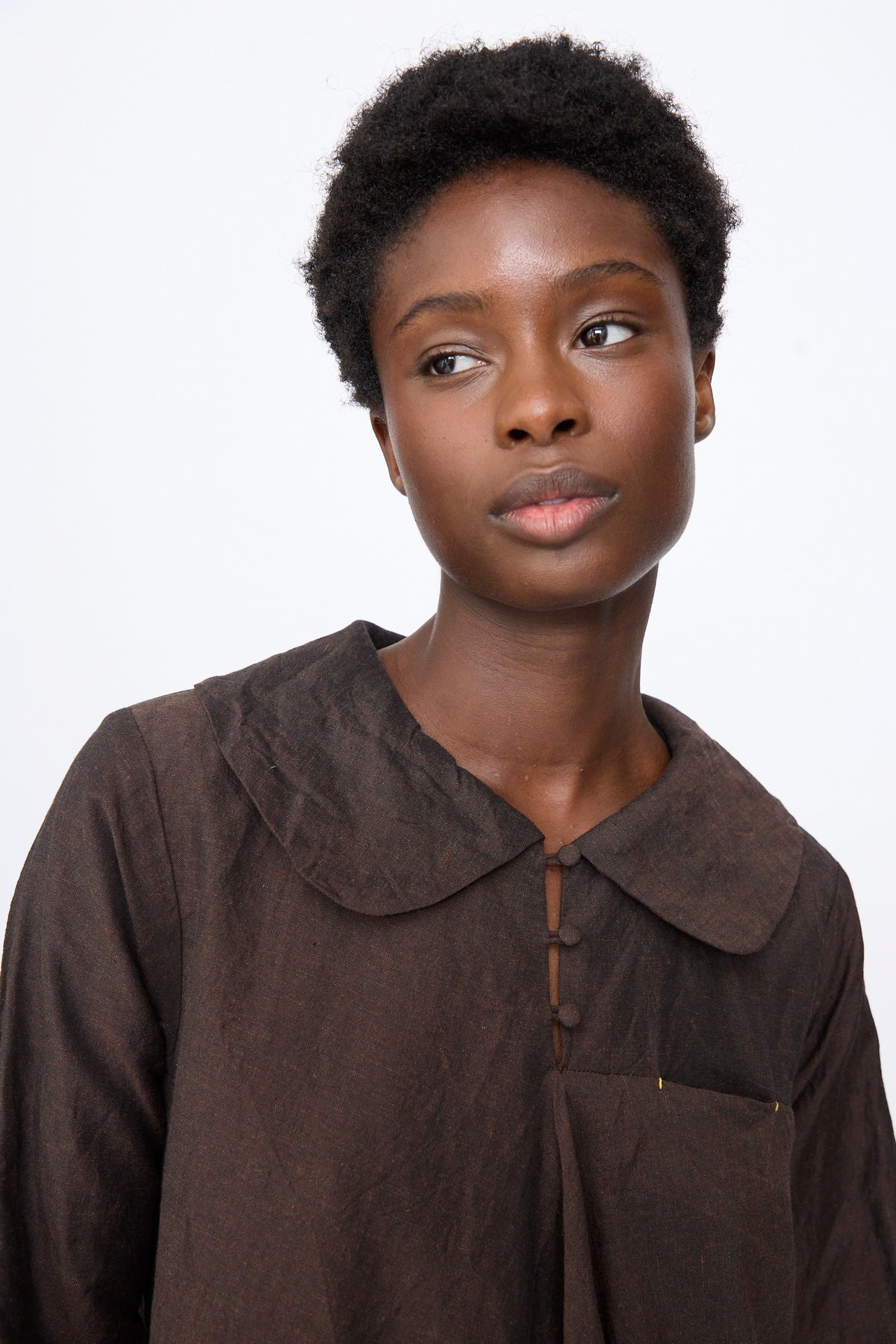A person wears a brown Hallelujah Linen Wool Robe à Col Claudine, a long-sleeve dress in a linen wool blend featuring a rounded collar and a small front button placket.
