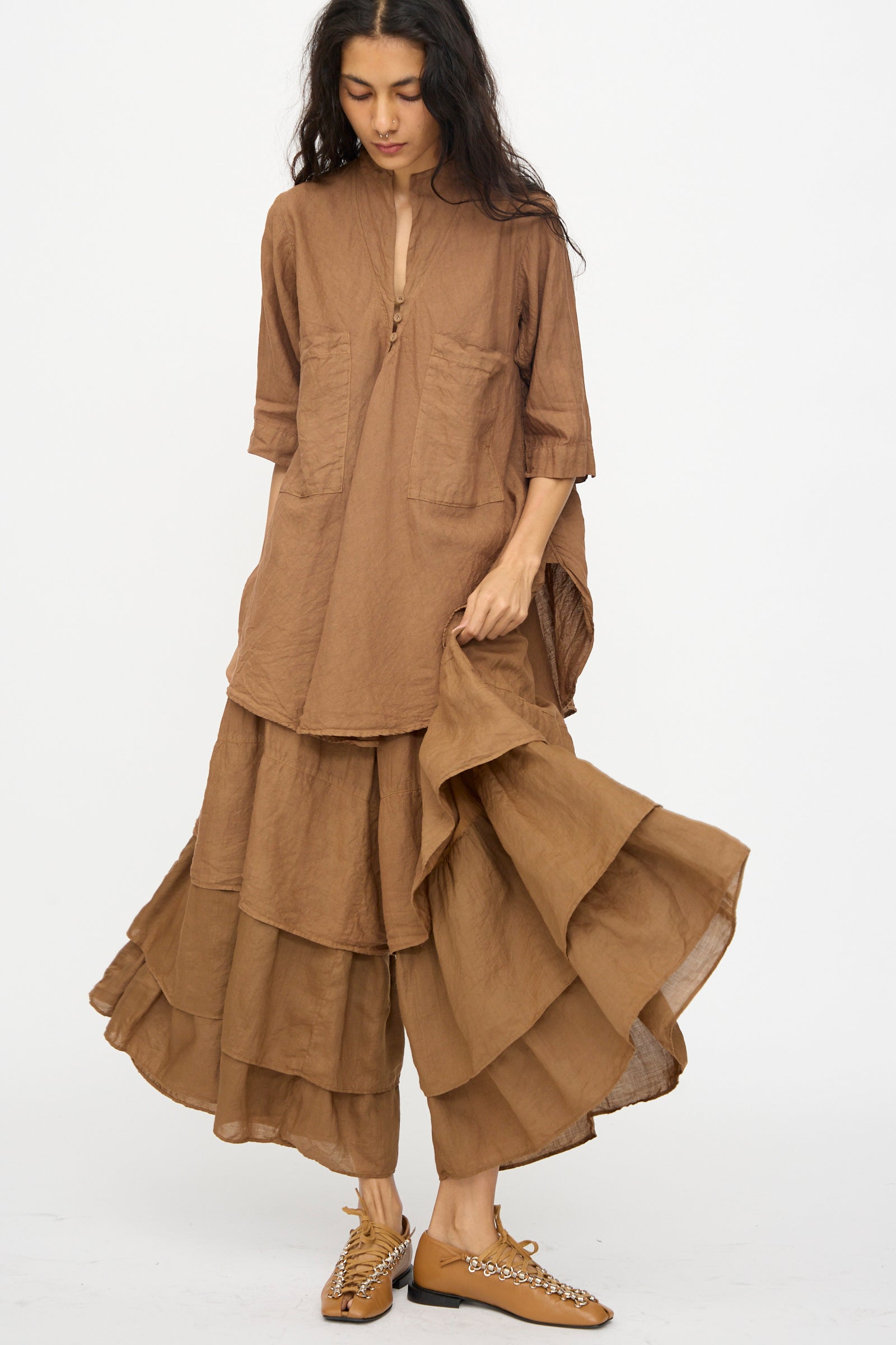 A woman models Hallelujah’s Pantalon Etagée in Persimmon Dye, pairing the cropped silhouette with tan embellished flats to highlight its effortless style against a plain background.