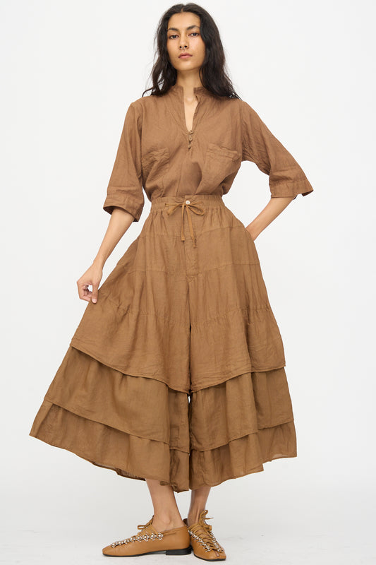 A person stands facing forward in Hallelujah's Pantalon Etagée in Persimmon Dye with tan shoes, set against a plain white background.