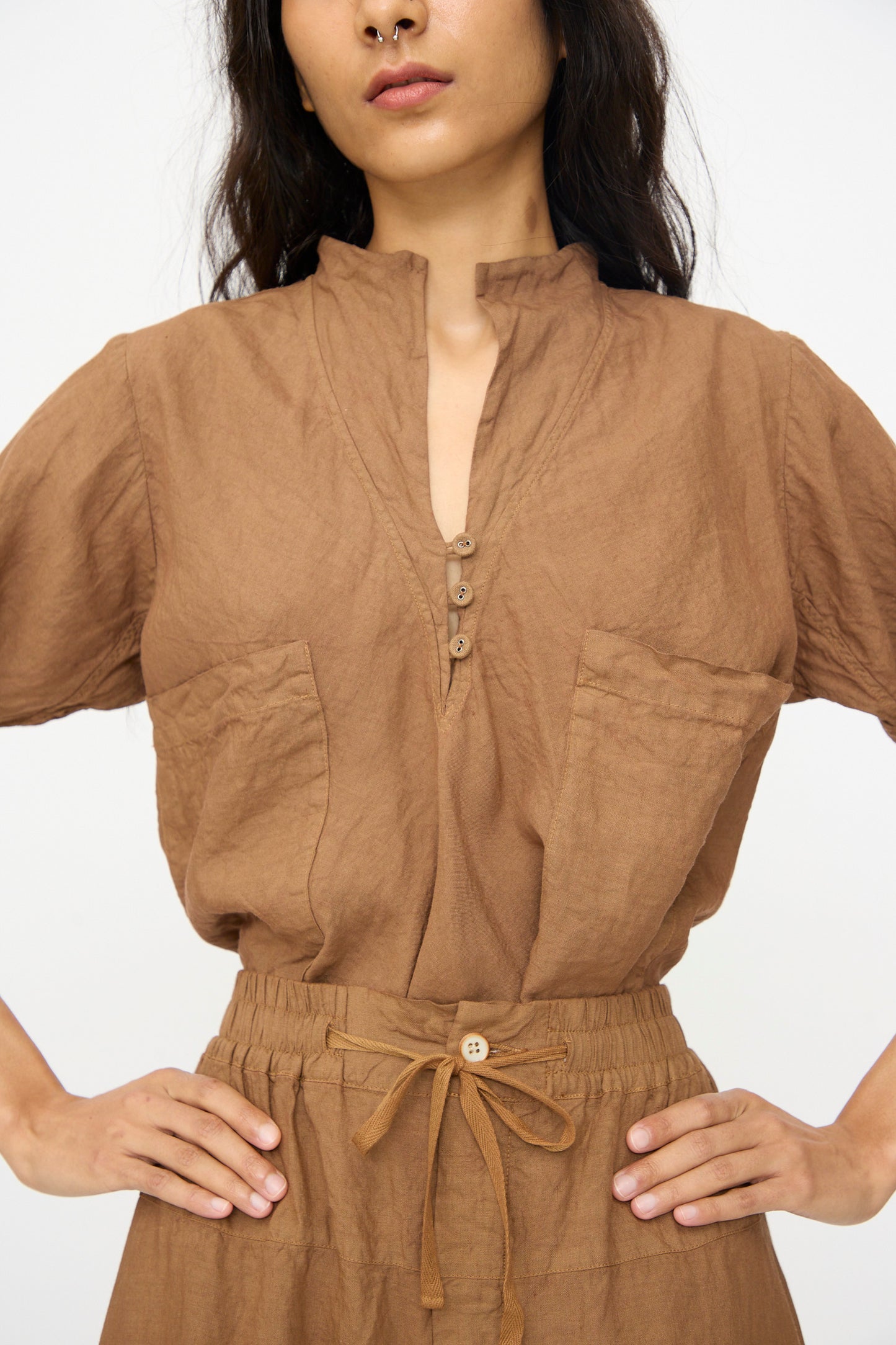 Woman wearing Hallelujah's Pantalon Etagée in Persimmon Dye, a stylish brown linen-ramie pant with large front pockets and a relaxed fit, hands on hips.