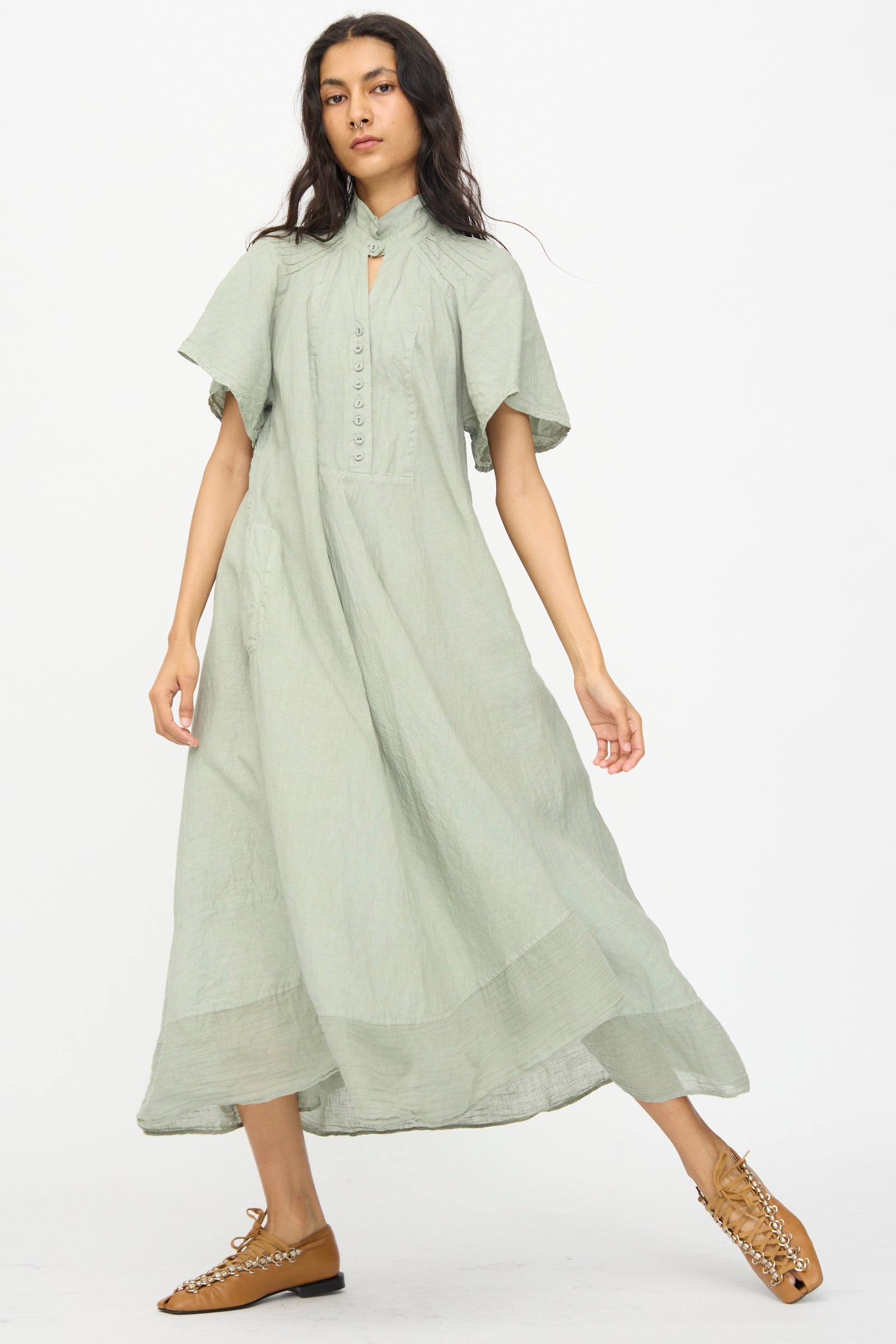 A woman in Hallelujah’s Robe 1900’s in Green Tea Dye, a loose ankle-length dress with short sleeves, stands against a white background wearing tan lace-up shoes.
