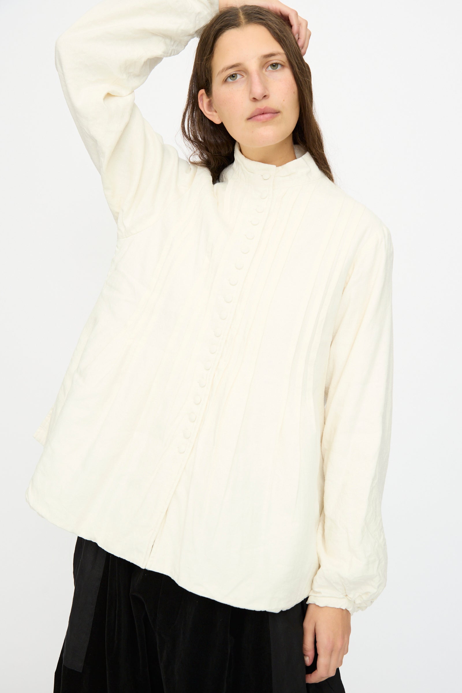 A person with long brown hair wears the Hallelujah Silk and Linen Chemise de Baptême in White and a black skirt, standing against a plain white background.