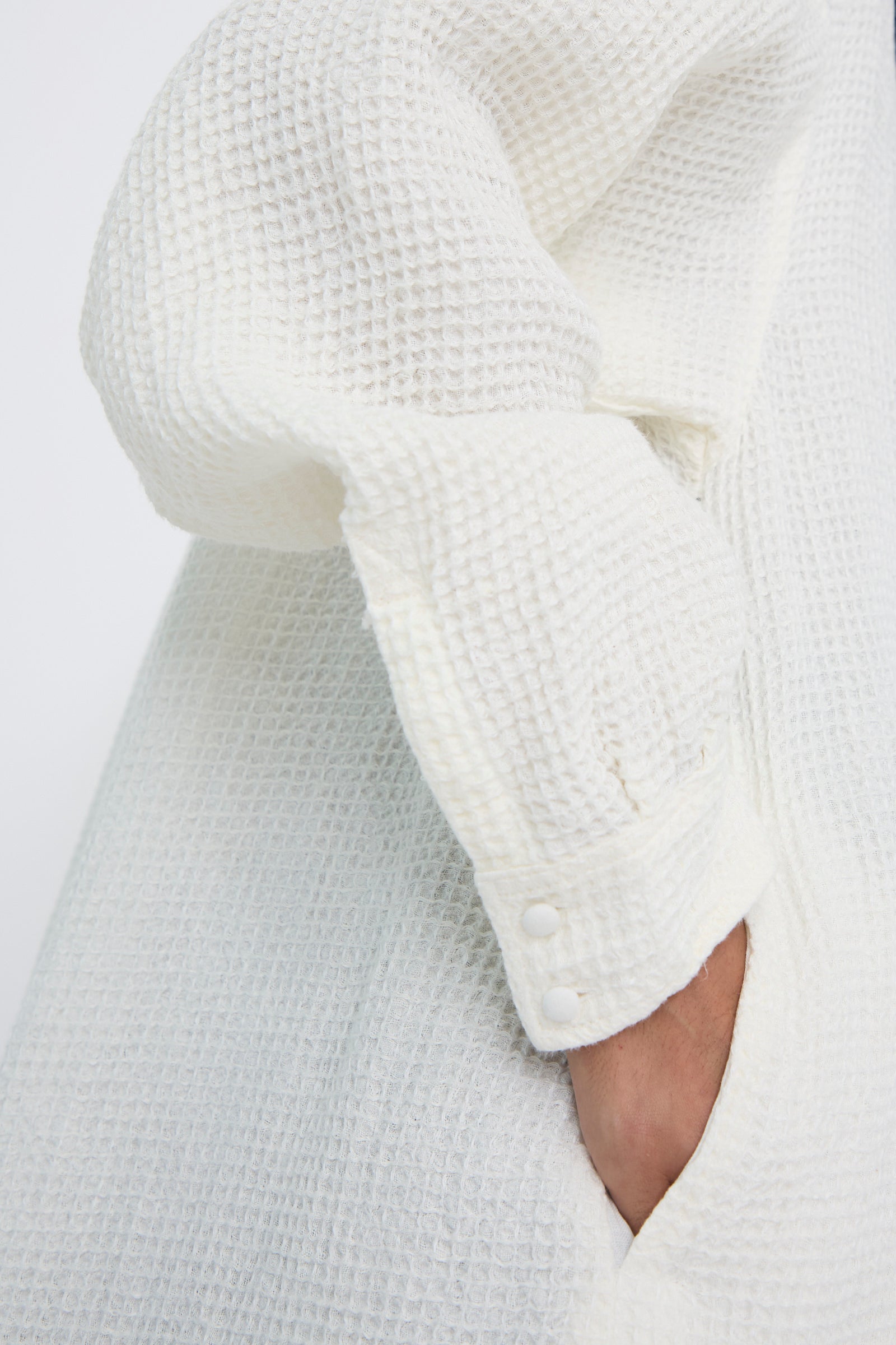 Close-up of a person wearing Hallelujah's Waffle Linen Robe Chemise in Milky White, their hand in a pocket. 