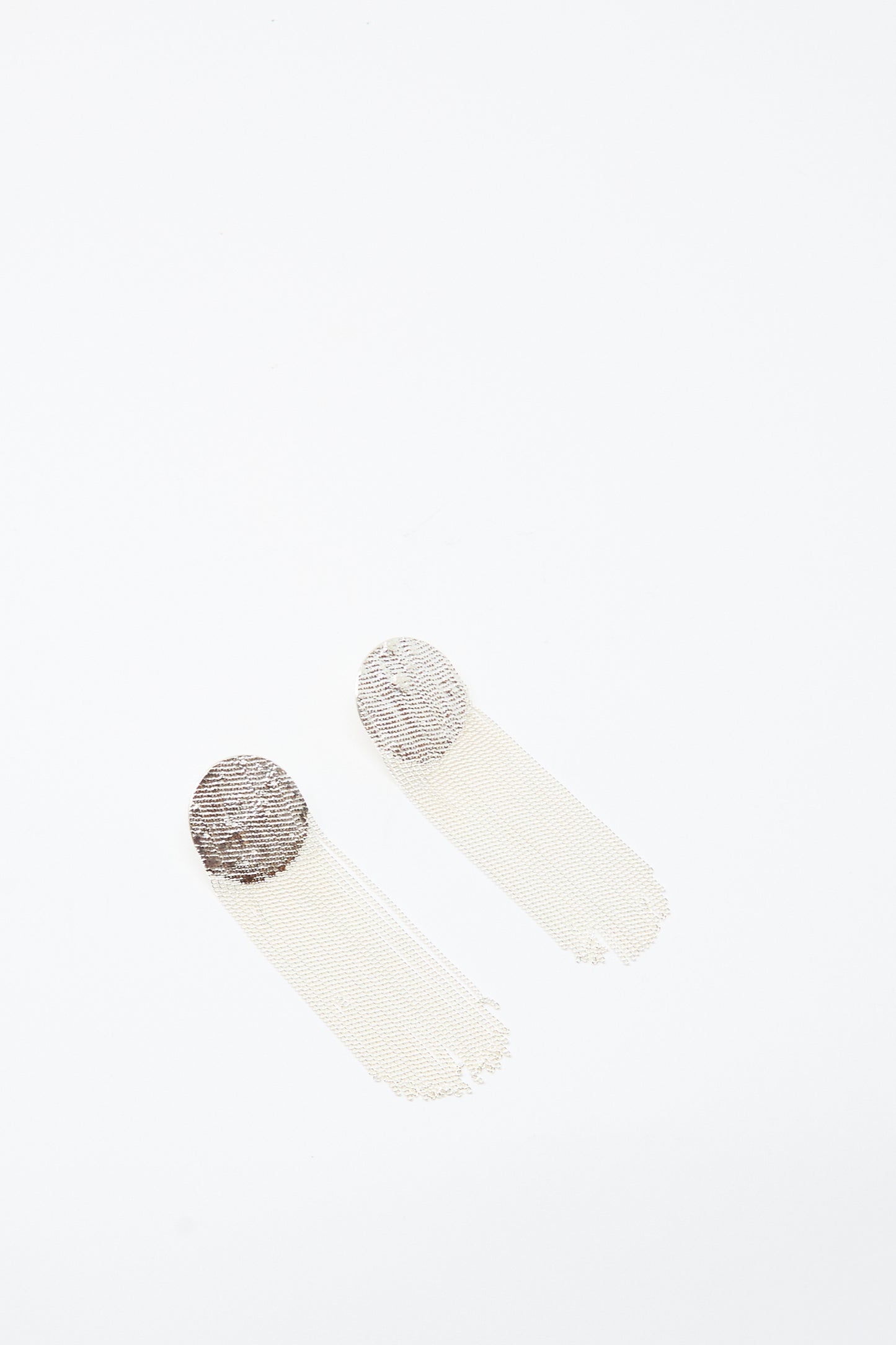 The Dot Earrings in Silver by Hannah Keefe feature handmade circular metallic tops with long, thin, mesh-style tassels, shown against a white background.
