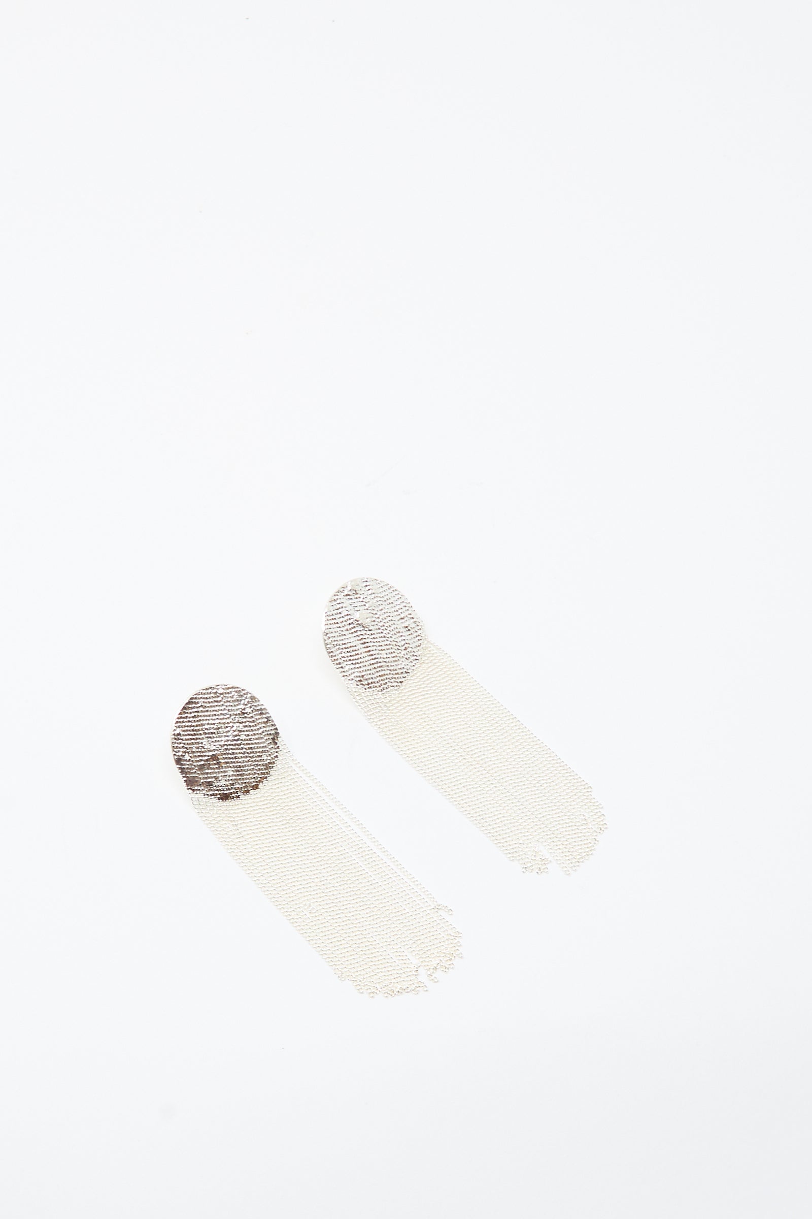 The Dot Earrings in Silver by Hannah Keefe feature handmade circular metallic tops with long, thin, mesh-style tassels, shown against a white background.