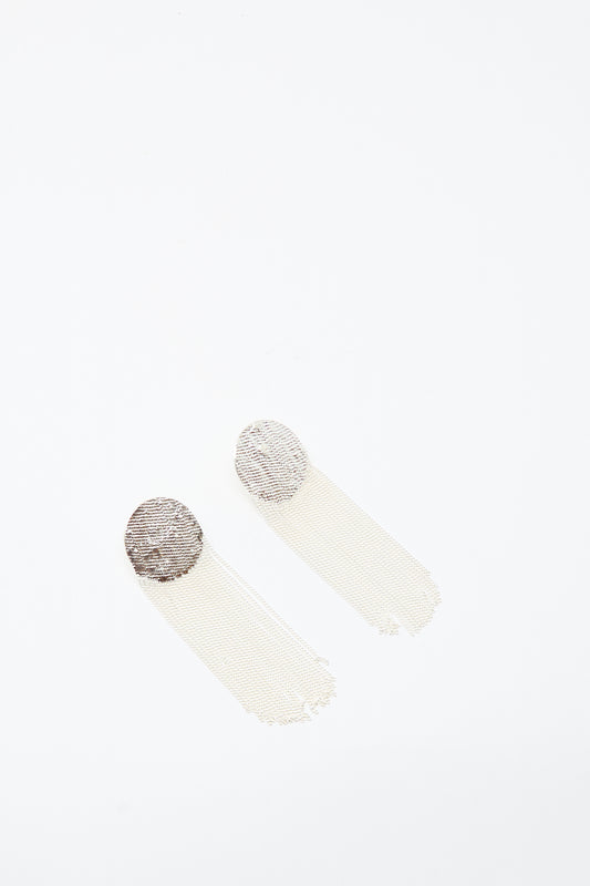 The Dot Earrings in Silver by Hannah Keefe feature handmade circular metallic tops with long, thin, mesh-style tassels, shown against a white background.