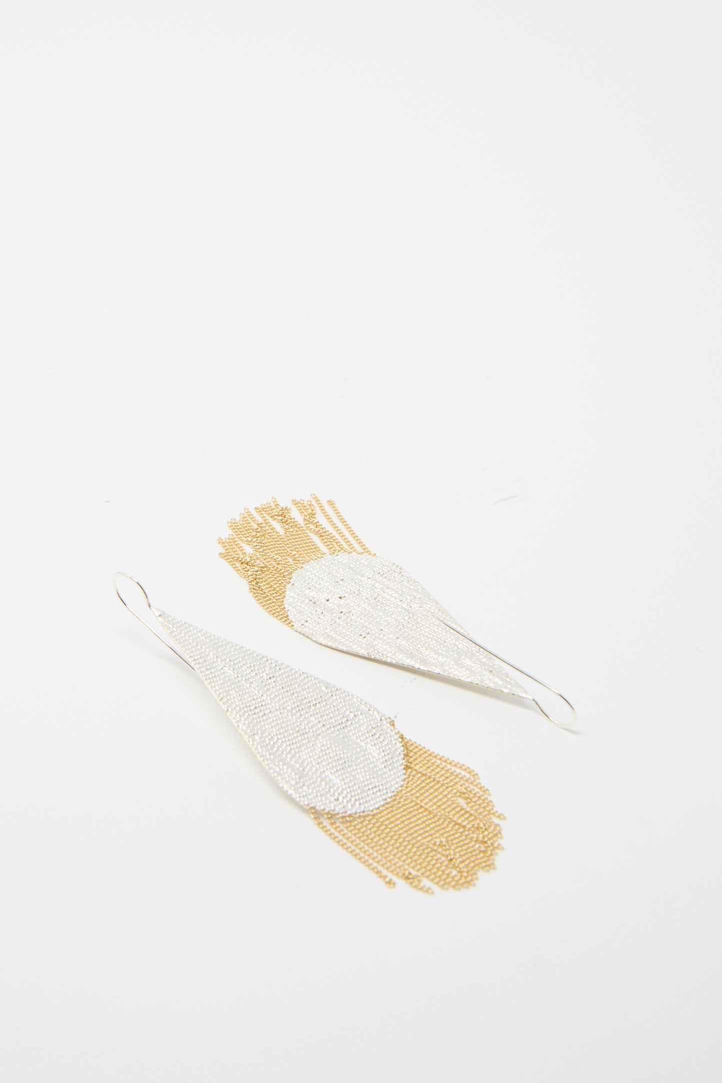 The Drip Earrings by Hannah Keefe showcase two teardrop silver designs with brass chain fringe, set against a plain white background. 