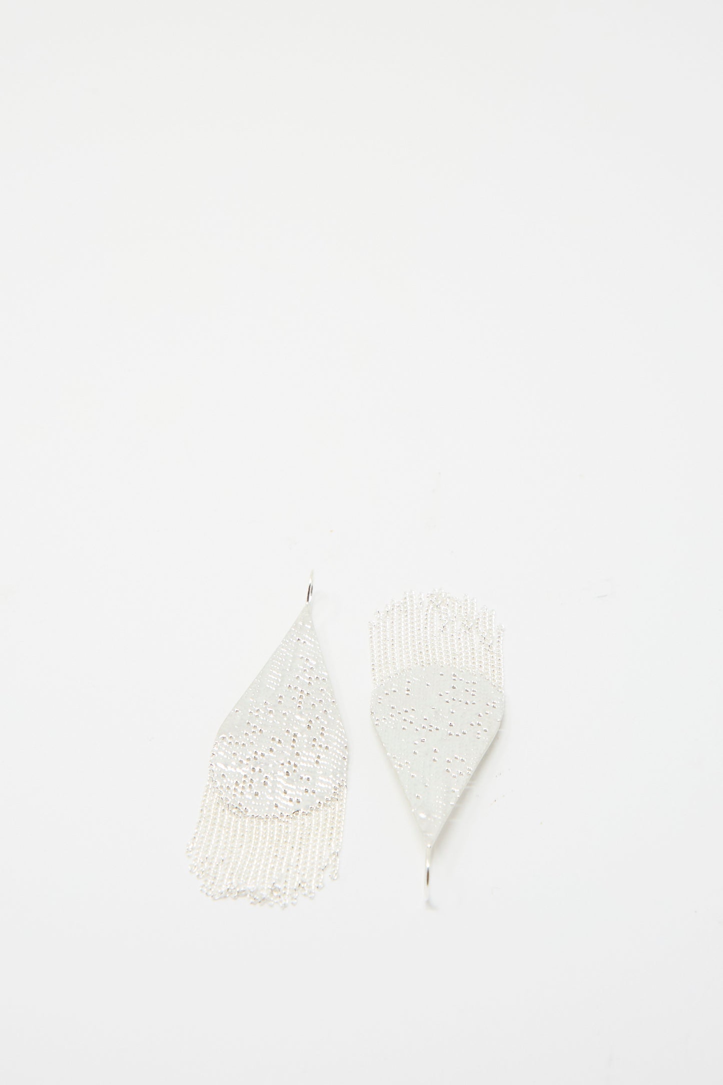 A pair of Drip Earrings in Silver by Hannah Keefe, featuring a teardrop shape with intricate cutout designs and a silver chain fringe, handmade in California, set against a plain white background.