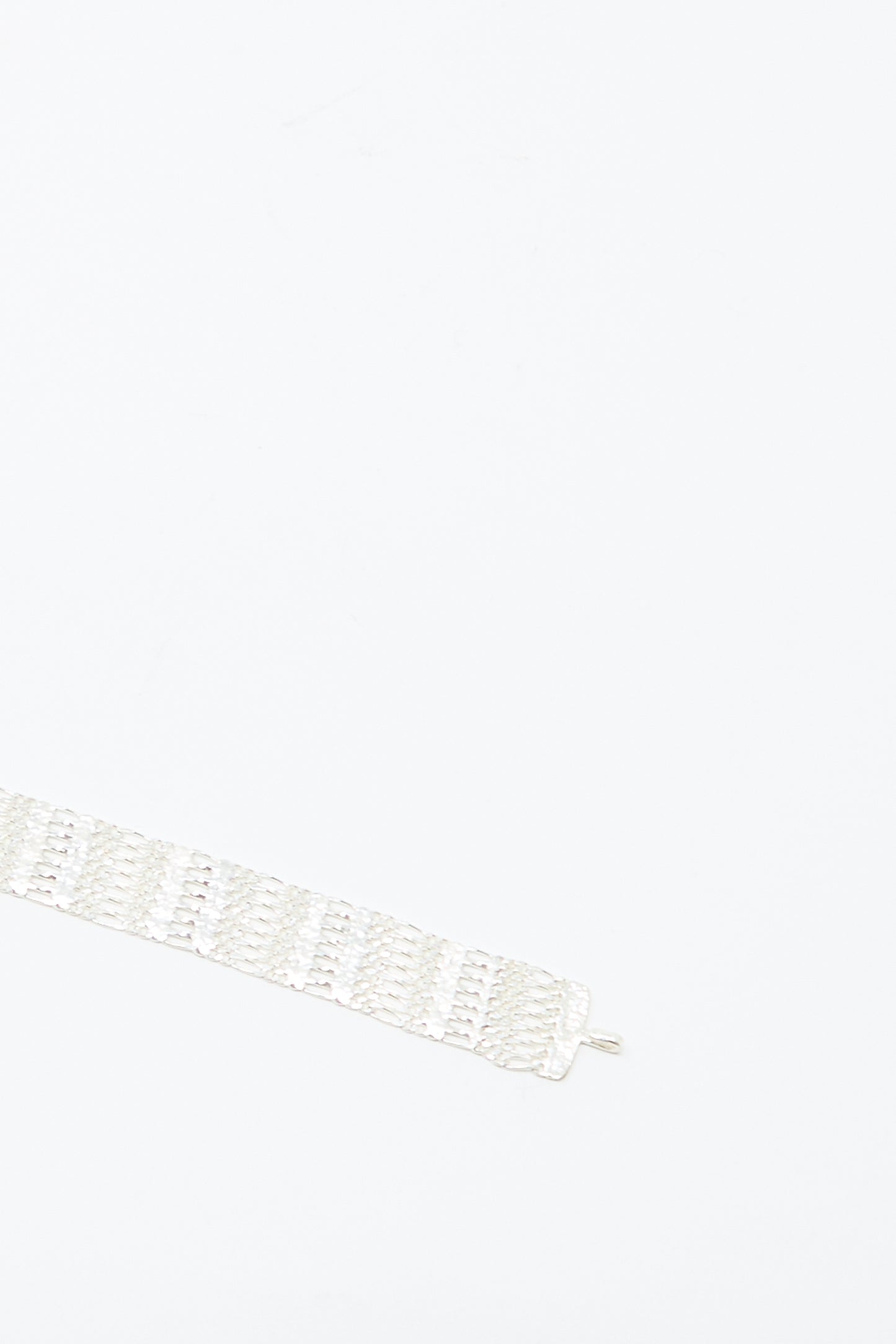 The Friendship Bracelet in Silver by Hannah Keefe, a wide handmade sterling silver chain with a textured pattern, is placed diagonally in the lower left corner on a plain white background.